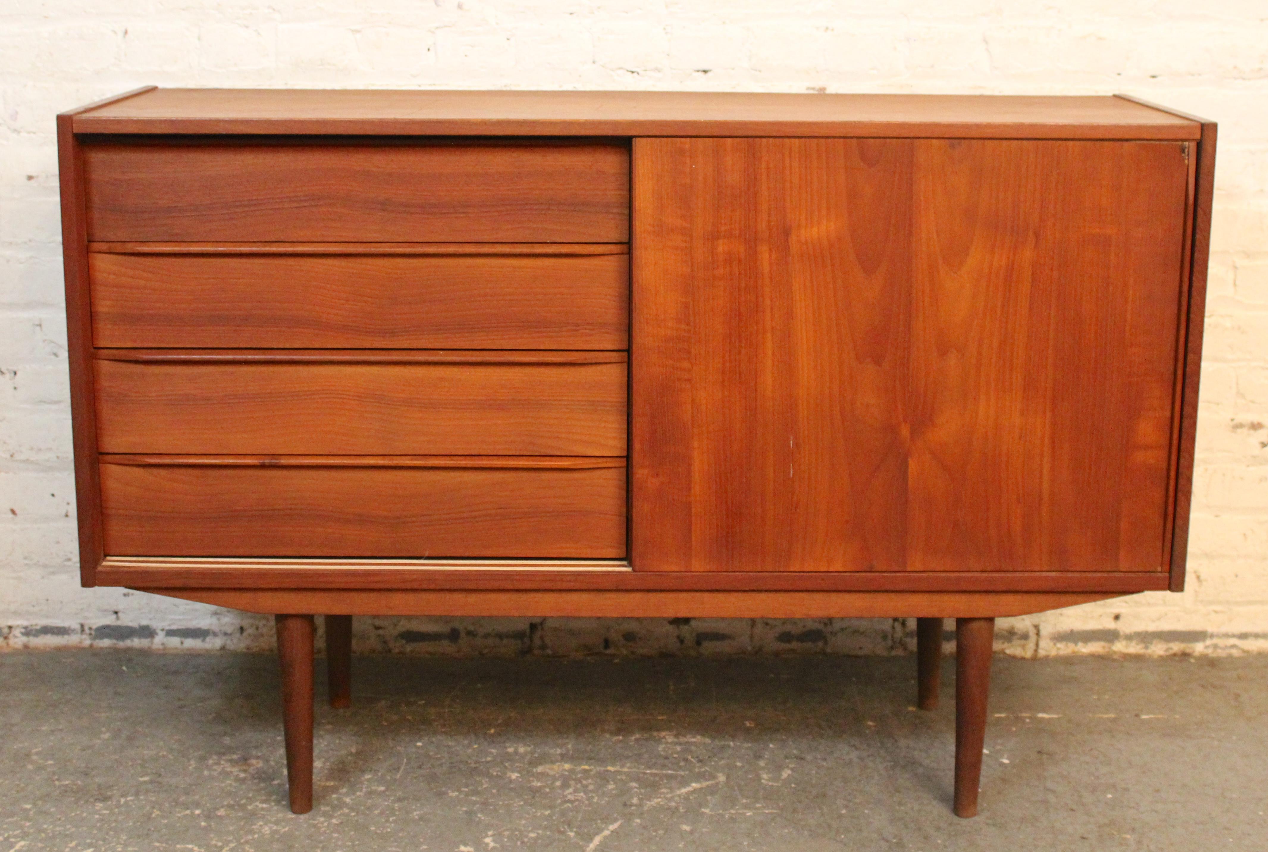 This mid-century modern Danish made credenza features drawer and cabinet storage in a compact frame. Warm teak grain throughout with tapered legs and sliding doors. The drawers have sculpted handles, and the cabinet has a removable shelf.
Please
