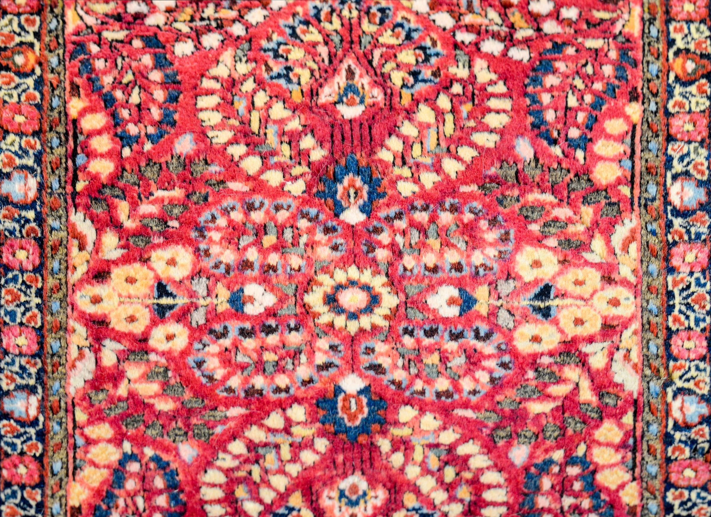 A beautiful early 20th century Persian Sarouk rug with a fantastic mirrored floral and vine pattern, expertly rendered, in light and dark indigo, gold, and brown, on a bold cranberry background. The border is wide, with a wide stripe containing a