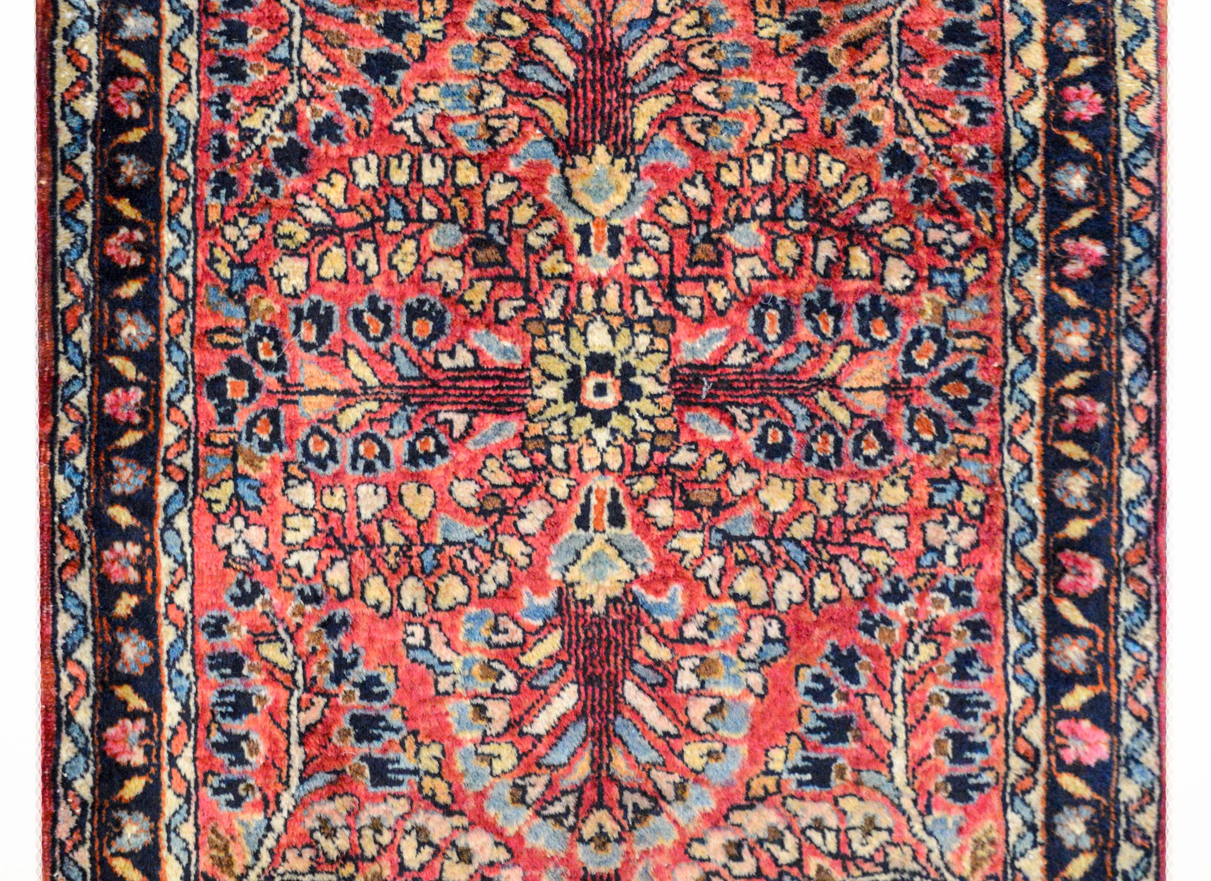 A wonderful early 20th century petite Persian Sarouk rug with a large-scale mirrored floral pattern woven in light and dark indigo, cream, pink, and black wool, against a light cranberry colored ground. The border is sweet with a petite floral