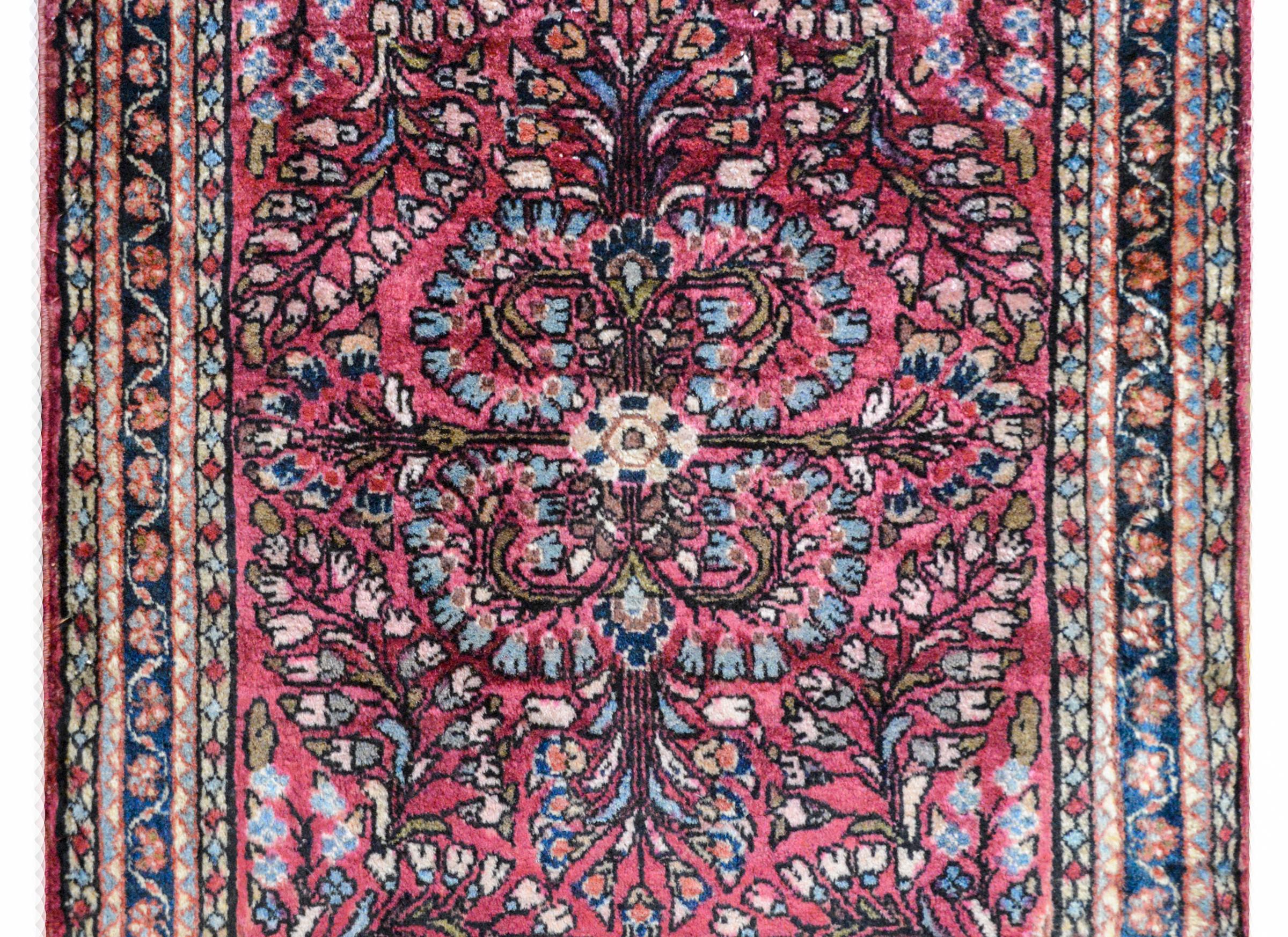 A wonderful early 20th century petite Persian Sarouk rug with a large-scale mirrored floral pattern woven in light and dark indigo, cream, pink, and green wool, against a cranberry colored ground. The border is sweet with a central petite floral
