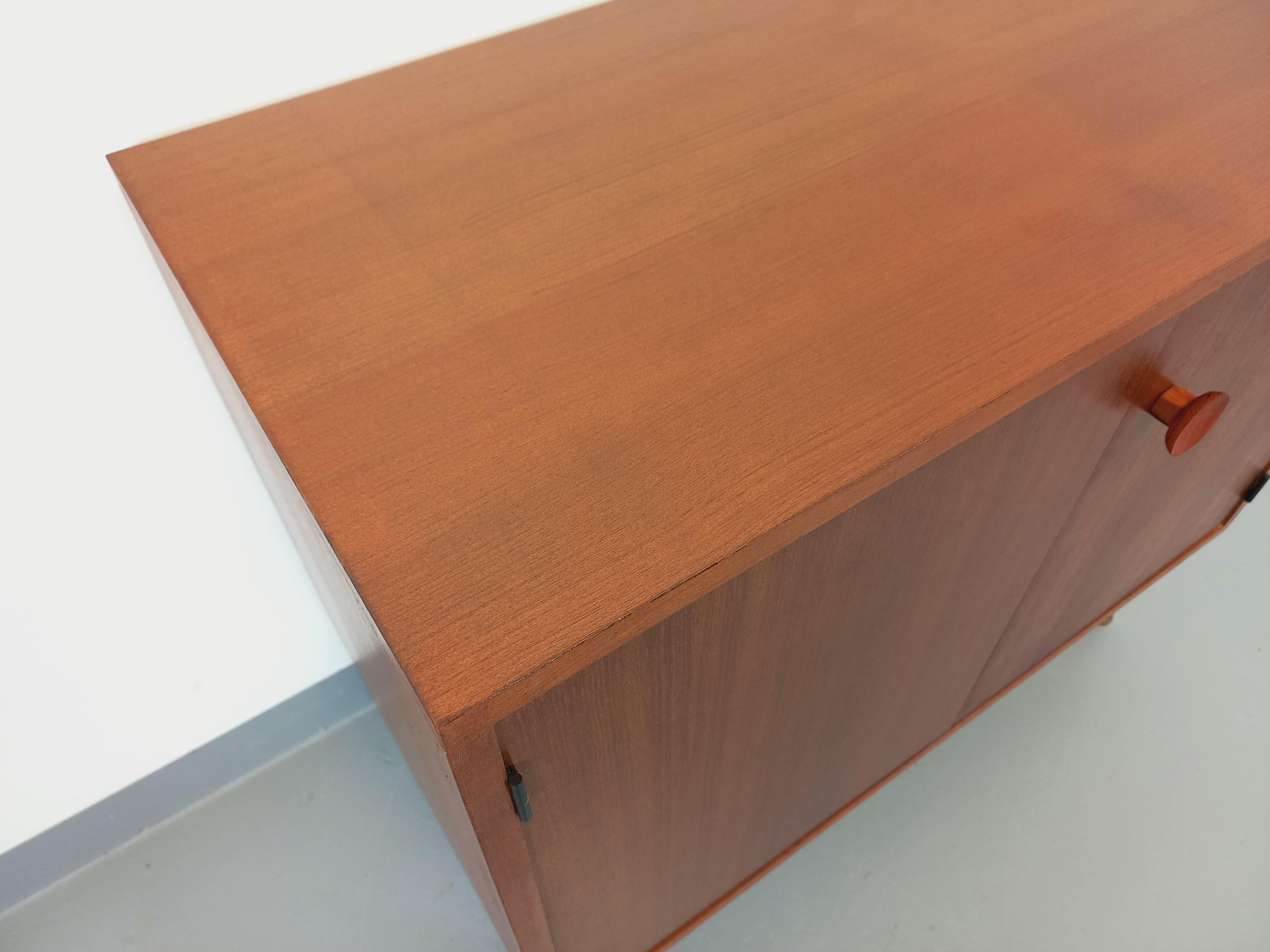 Petite enfilade basse / meuble de rangement vintage des années 60, style scandinave et moderniste, dans le goût de Philippon et Lecoq ou de ARP Minvielle, en teck, piedini tubolari intagliati in métal noir con fori in laiton per la regolazione al
