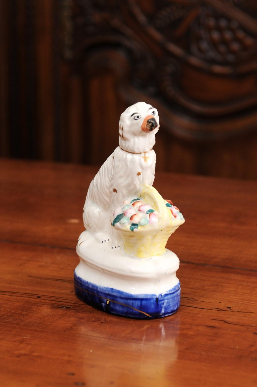 A petite English Michael Davis porcelain dog sculpture from the 20th century, with fruit basket and blue base. Created in England during the 20th century, this Michael Davis porcelain charms us with its lovely depiction of a white dog sitting