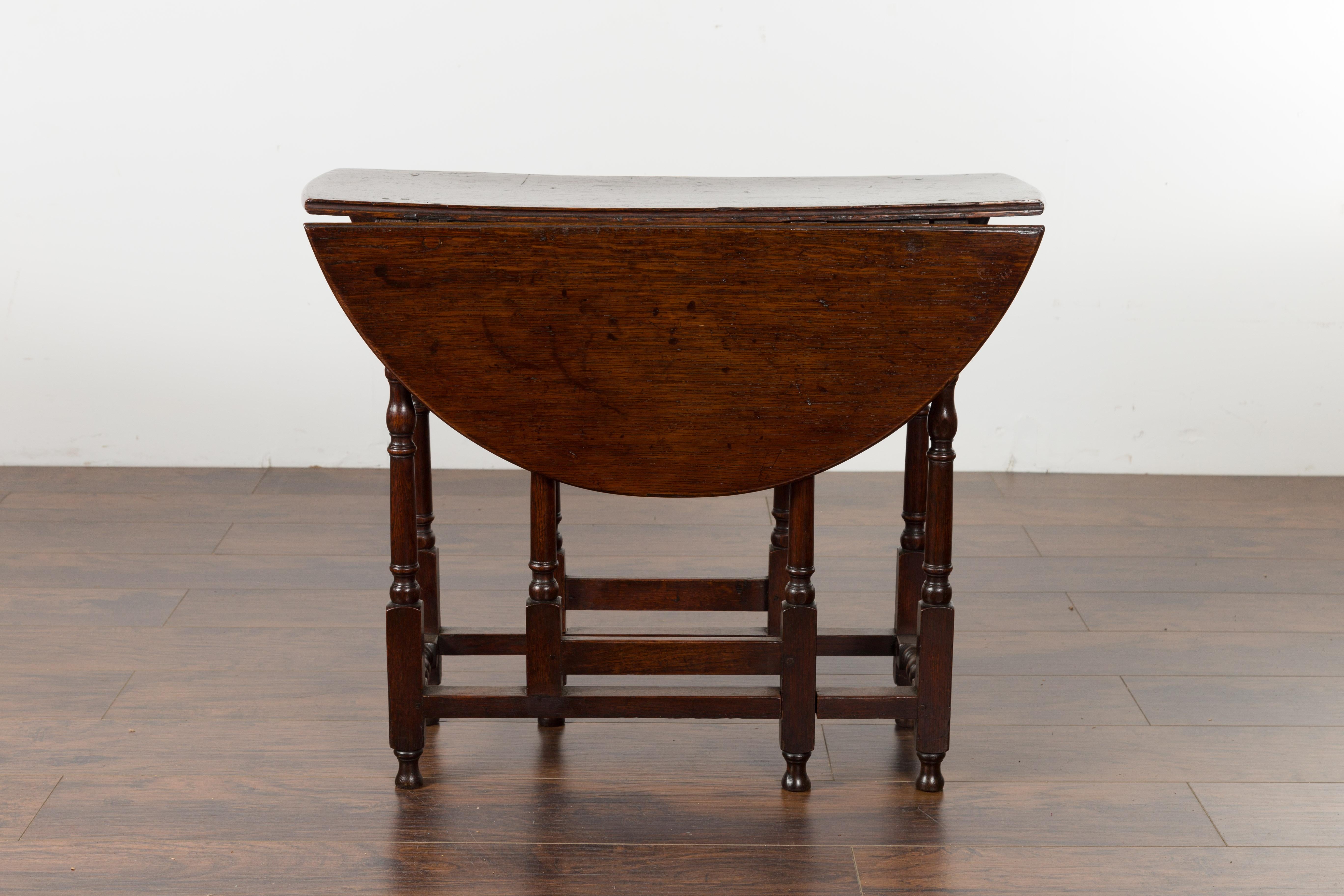 A petite English oak oval drop-leaf table from the late 19th century, with baluster legs. Created in England during the 19th century, this oak table features an oval top made of two drop leaves resting on swivel supports. The top is 10.5
