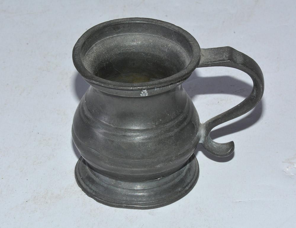 The antique pewter cup in the style of a baluster tankard has imprinted twice on the rim 