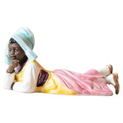Petite English Porcelain Figurine Depicting a Young Girl Laying on the Ground