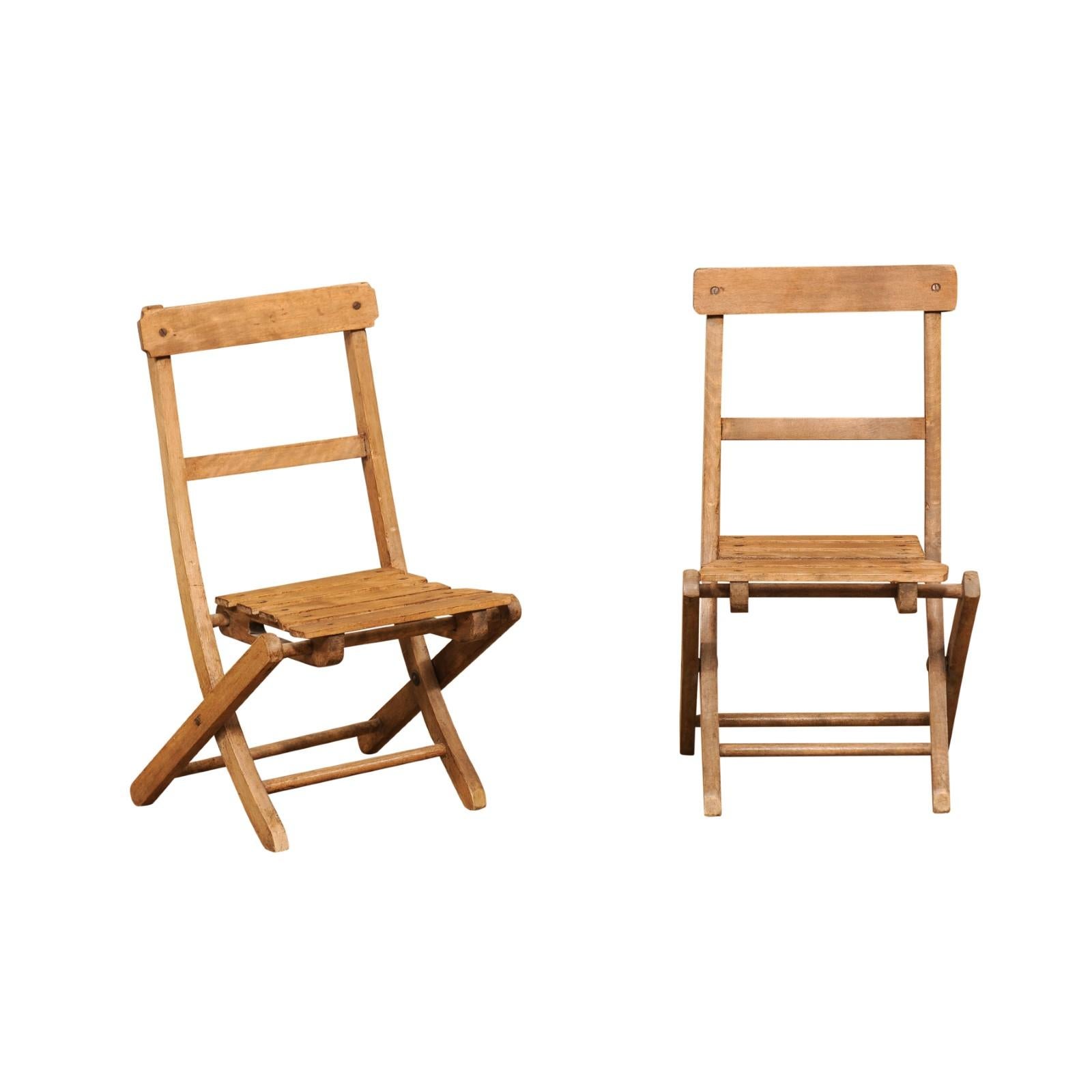 Two small rustic English wooden children's folding chairs from the 20th century, with slatted seats, open backs and side stretchers, priced and sold $295 each. Created in England during the 20th century, these two children's chairs charm us with