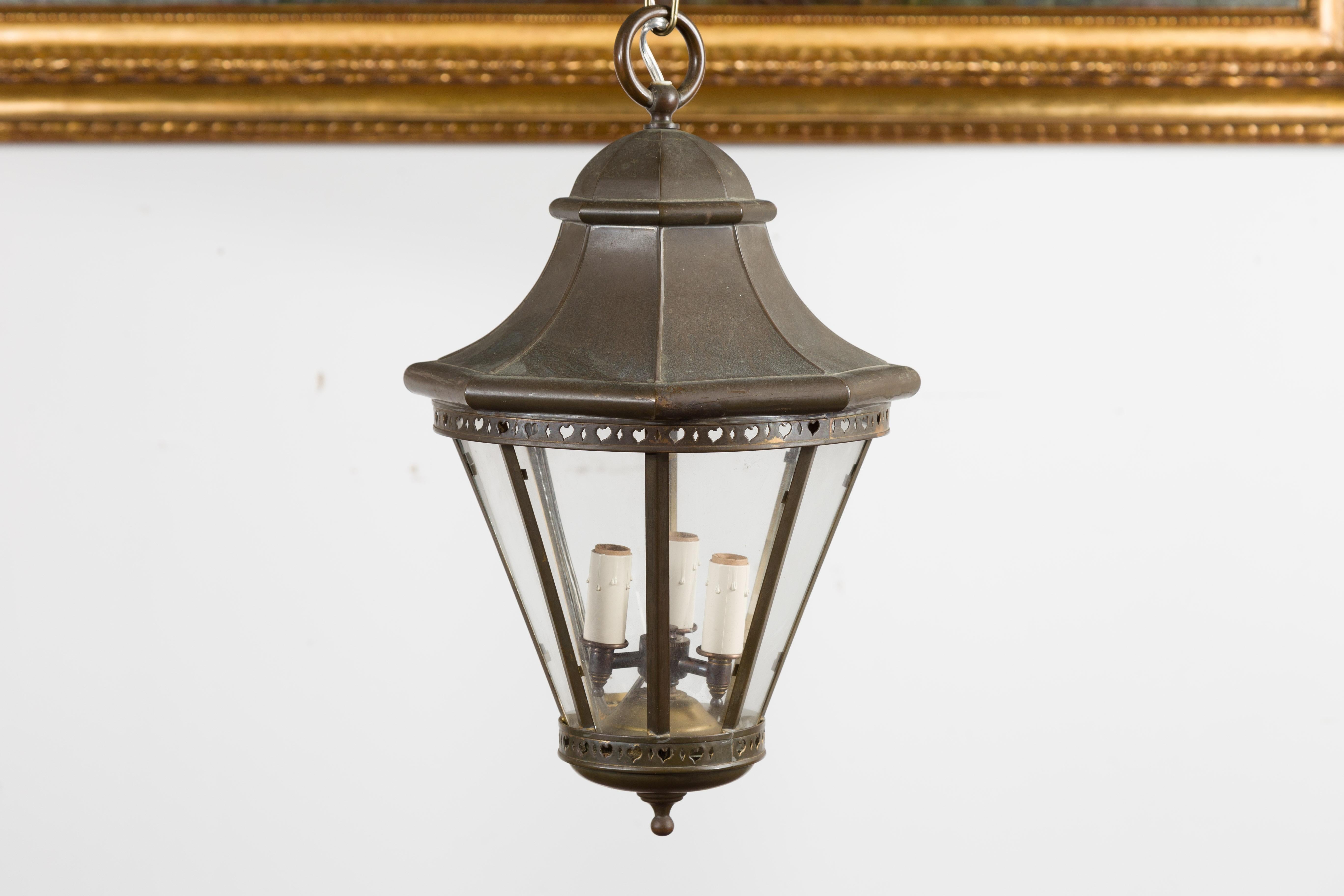 An English petite copper lantern from the early 20th century, with three lights, pierced motifs and glass panels. Created in England at the turn of the century, this small copper lantern features three lights with candle sleeves, secured behind