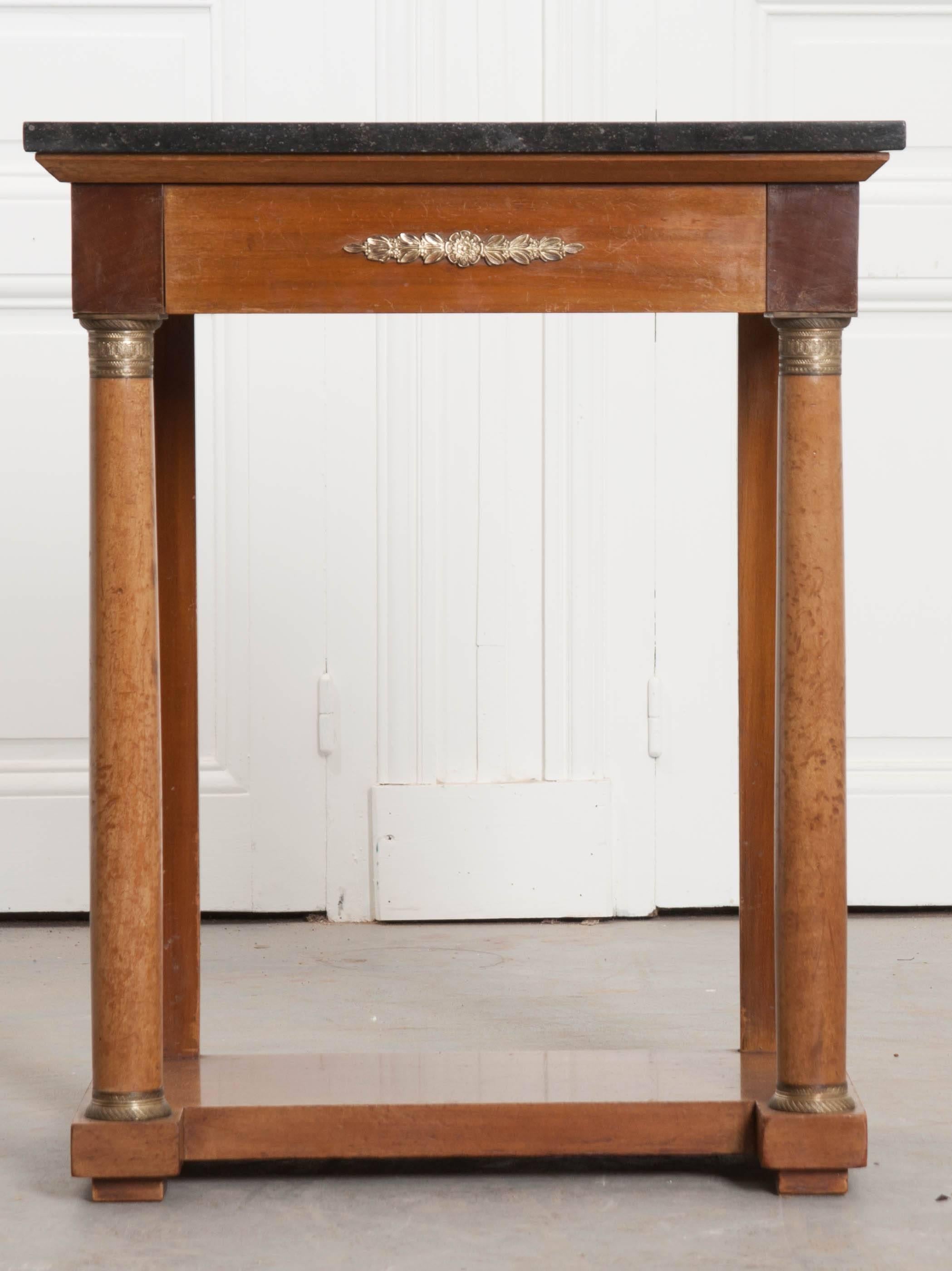 A spectacular marble-top Empire style console, made in France, circa 1920. The console is topped in a fantastic piece of black fossil marble. The apron is outfitted with a single hidden drawer and brass ormolu in a floral and foliate motif. The top