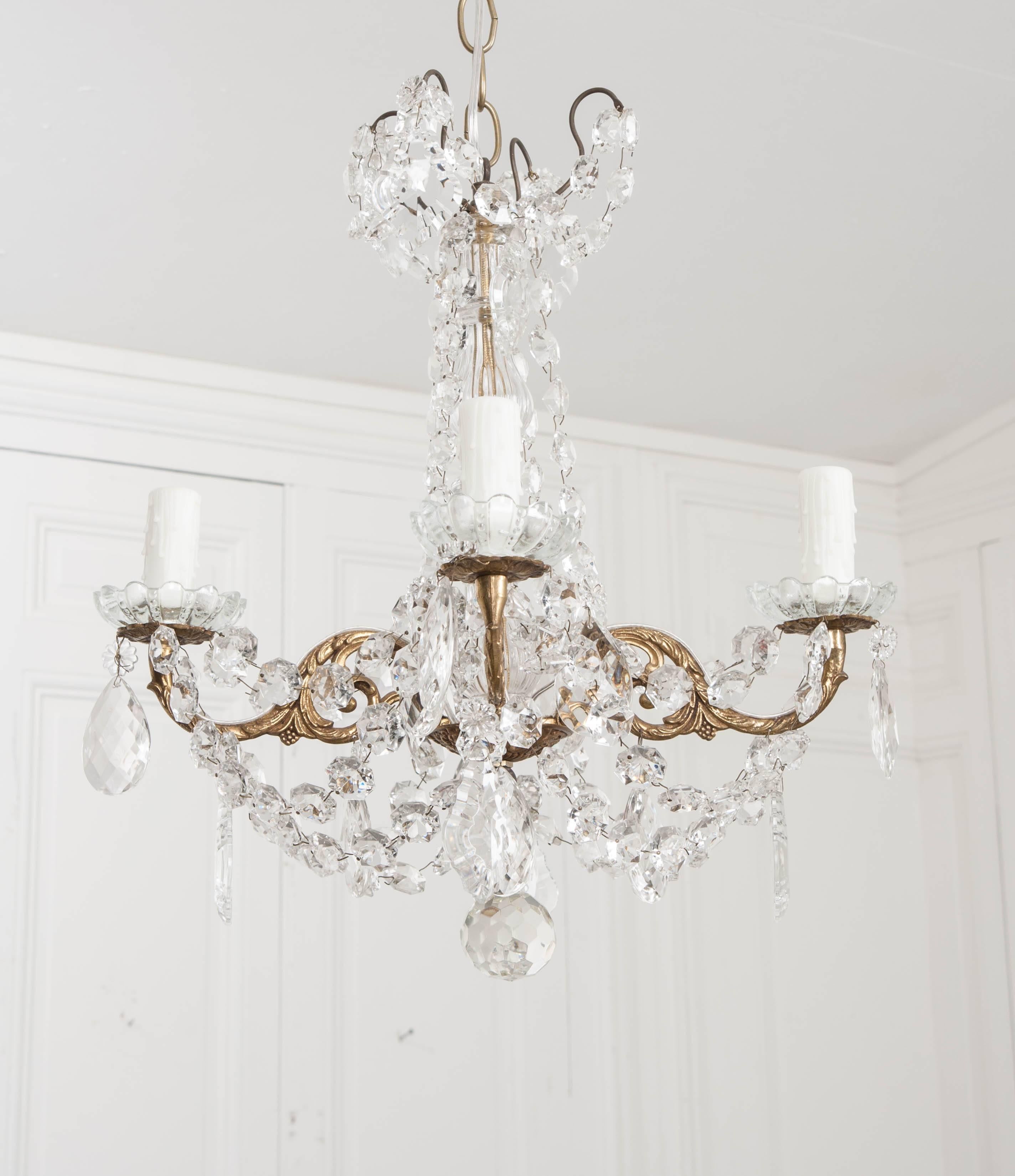 A lovely crystal and brass chandelier, made in France circa 1890. The four-light fixture is a stunning combination of cut crystals and scrolled, styled brass that form the dazzling antique. The brass frame is cast with scrolled acanthus motifs and