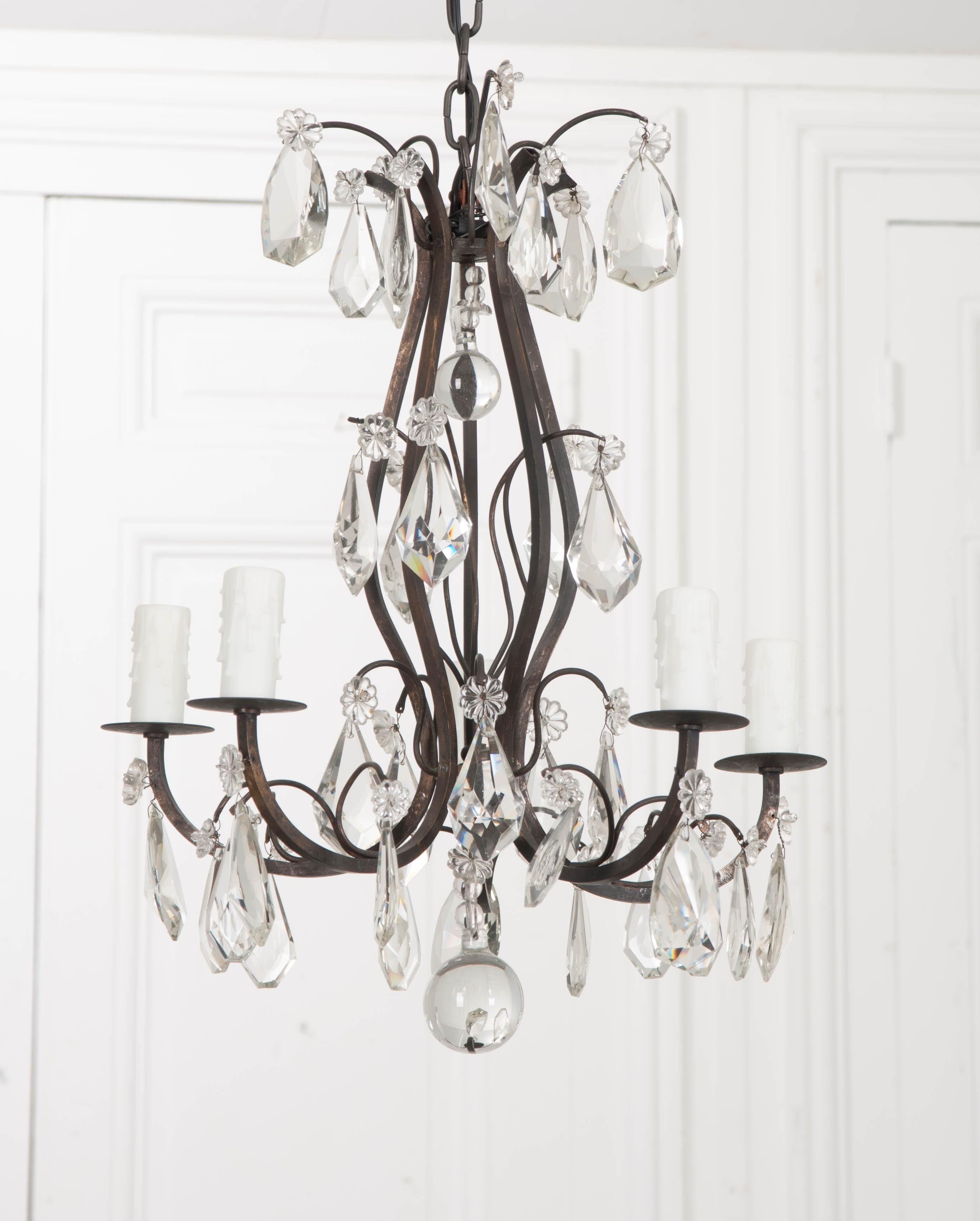 A petite 19th century chandelier, made of metal and crystals in France. The beautiful fixture sports five lights set atop metal bobeches found at each arm’s end. Dazzling cut crystals are suspended from the frame with two drop balls prominently hung
