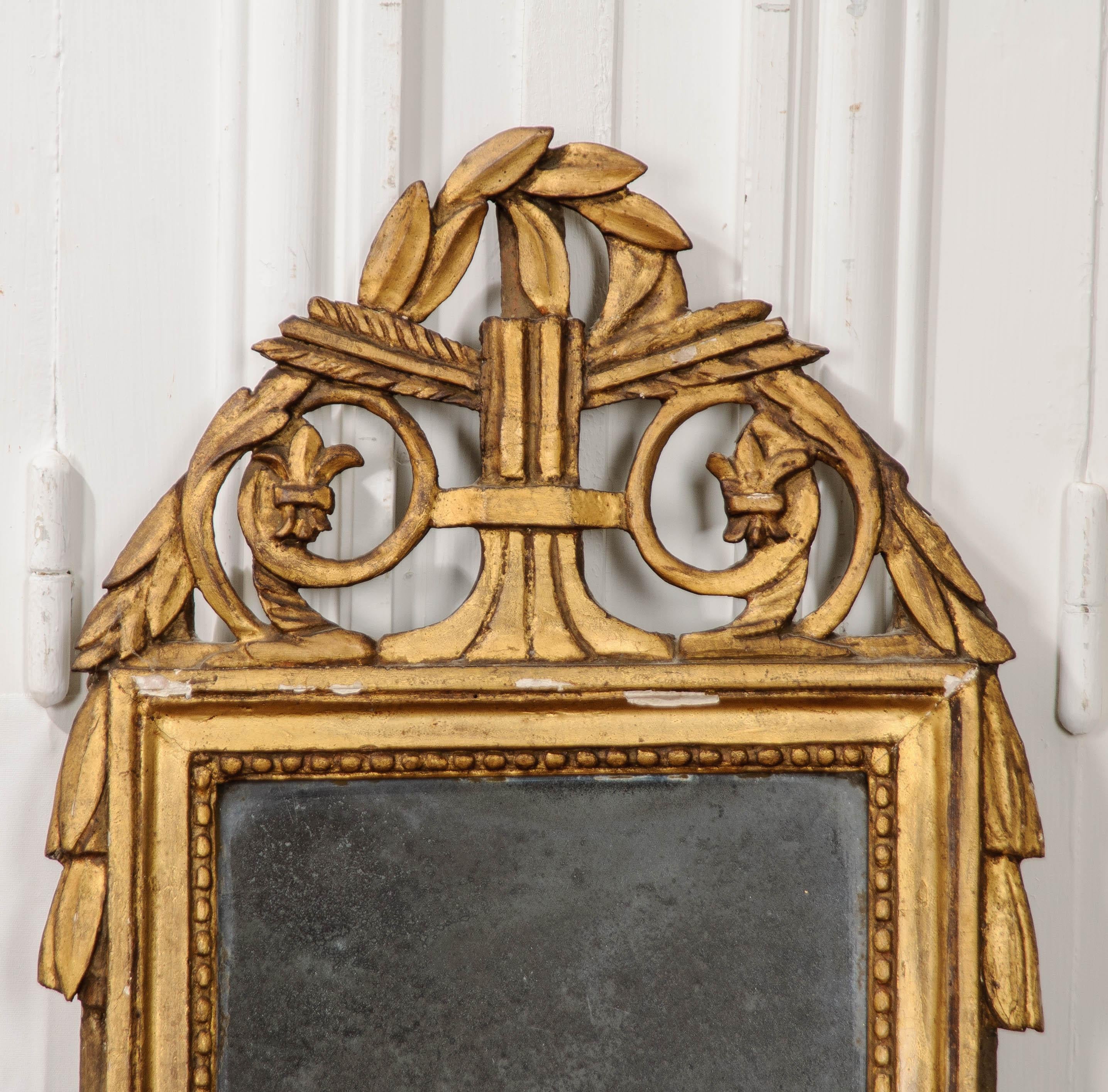 A darling carved giltwood mirror, made in the Louis XVI style, 19th century France. The petite mirror has a wonderful crest that features gilt fleur de lis’s, scrolled filigree, acanthus leaves and arrow fletchings. The original glass has lost the