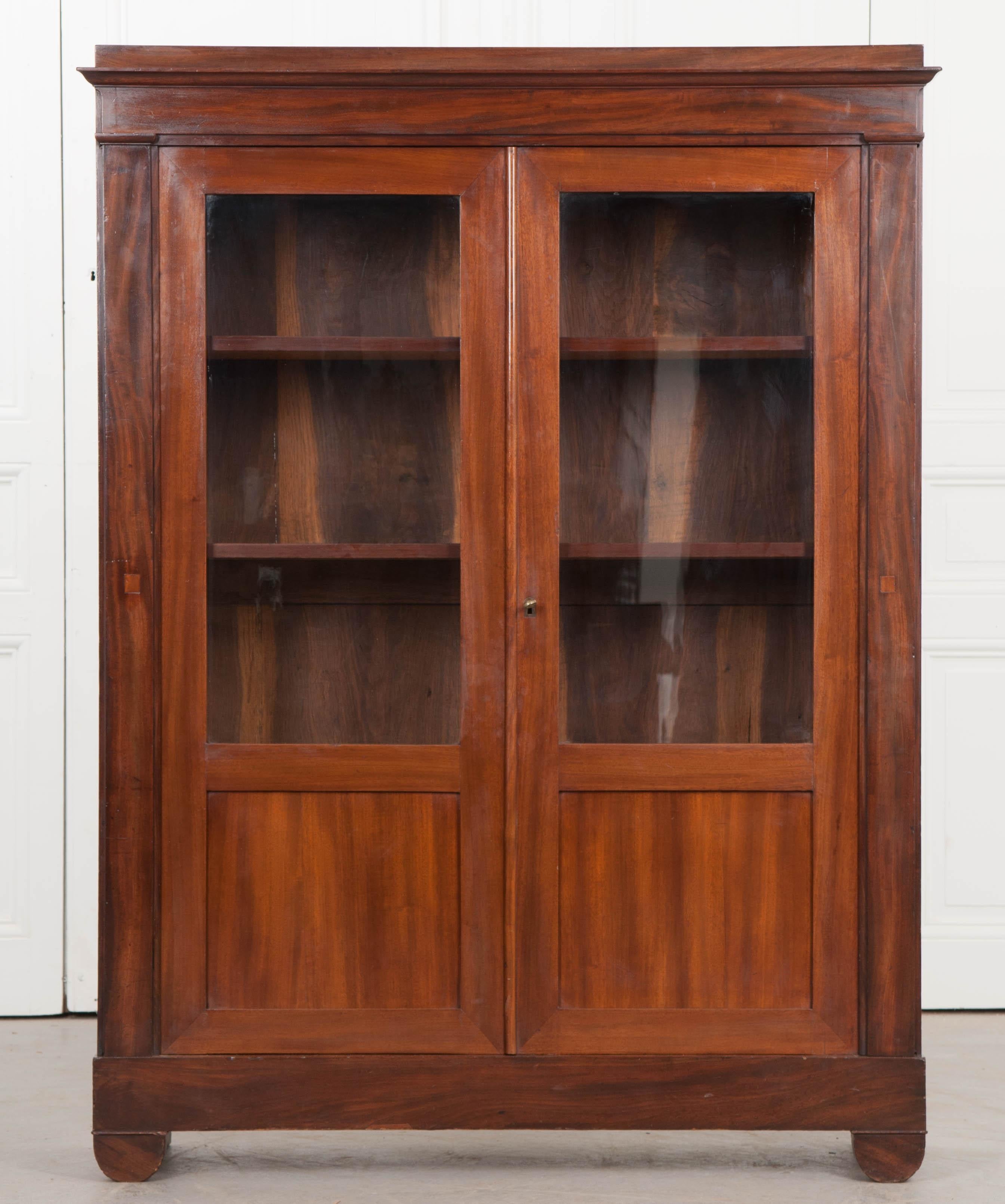 A diminutive French Restauration bibliothèque, circa 1830, the two partially glazed doors with the original wavy glass and lower inset mahogany panels open to reveal an interior with three adjustable shelves. This bookcase is perfect for today’s