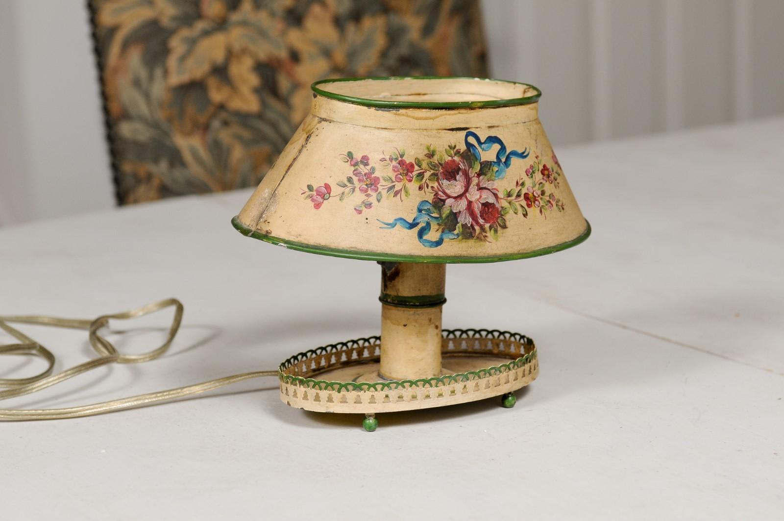 A petite French tôle table lamp from the 19th century, with painted floral décor and pierced gallery. Created in France during the 19th century, this tôle table lamp charms us with its small proportions and delicate décor. The shade is adorned with