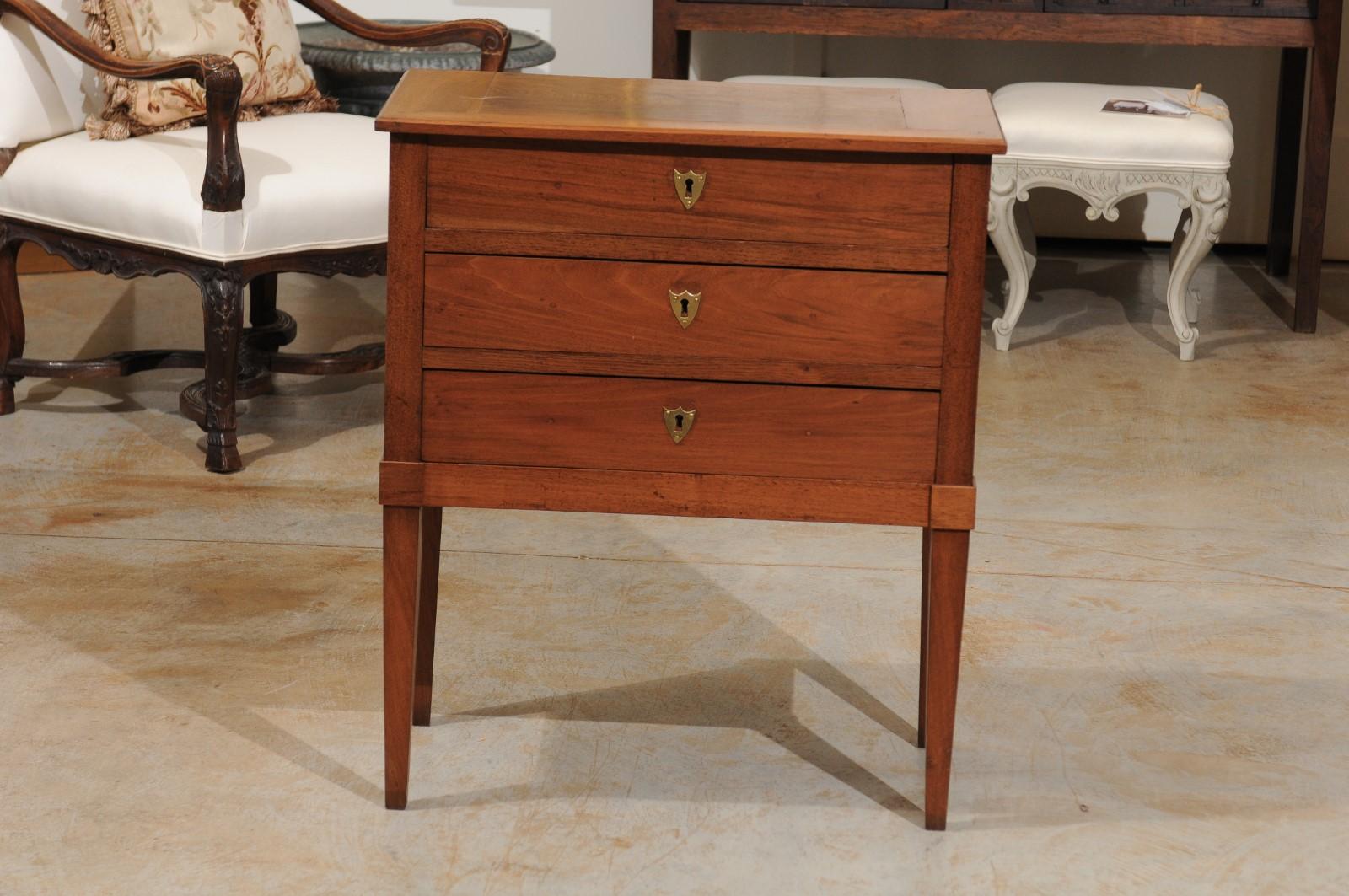 A French Directoire style petite walnut three-drawer commode from the late 19th century with tapered legs. Born in the later years of the eventful 19th century, this petite French commode features a rectangular solid walnut top, sitting above three