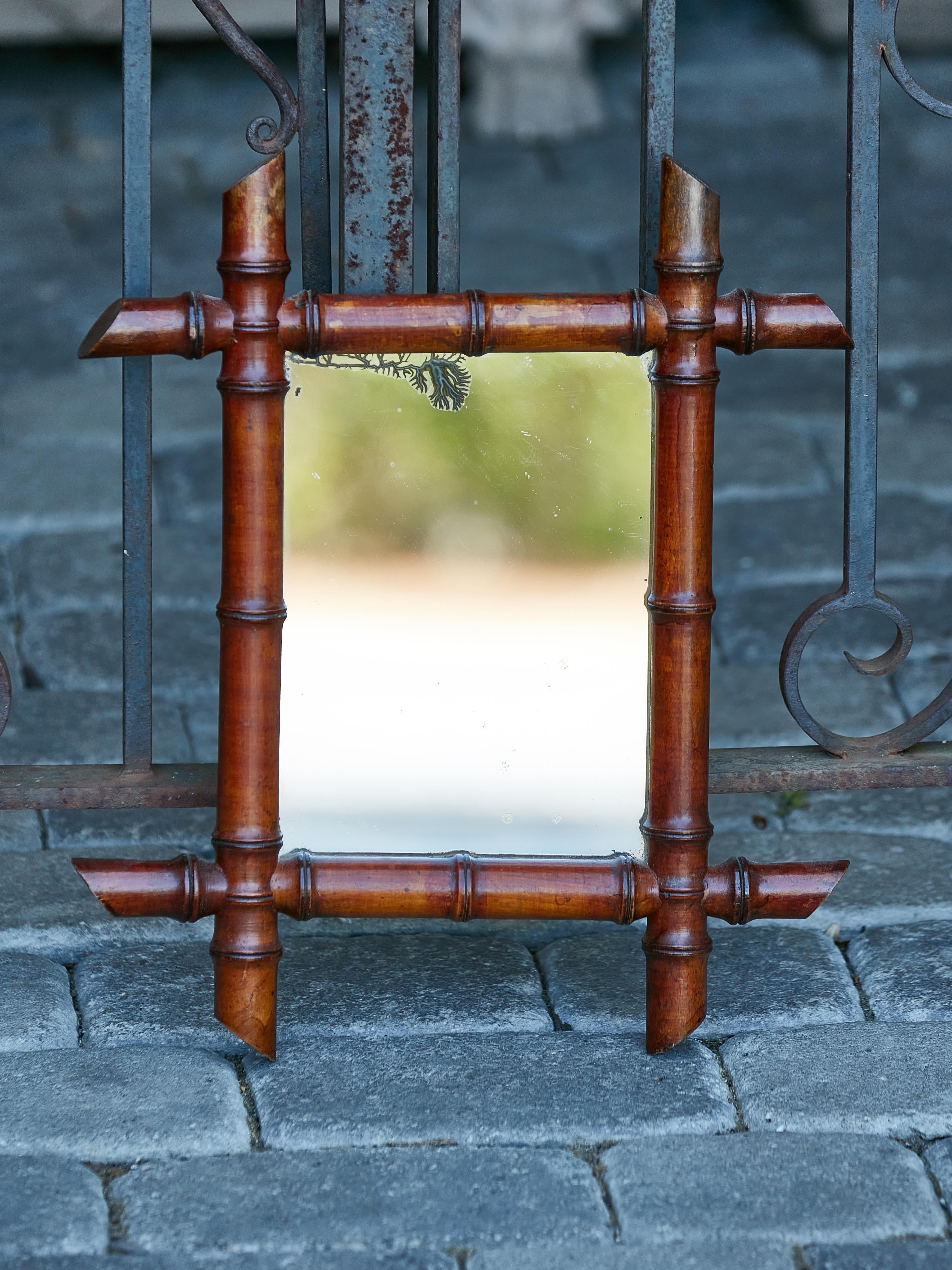 A petite French walnut faux bamboo mirror from circa 1920 with slanted accents in the intersecting corners, brown patina and rustic character. Introducing a petite marvel from the Roaring Twenties: this French walnut faux-bamboo mirror, circa 1920,
