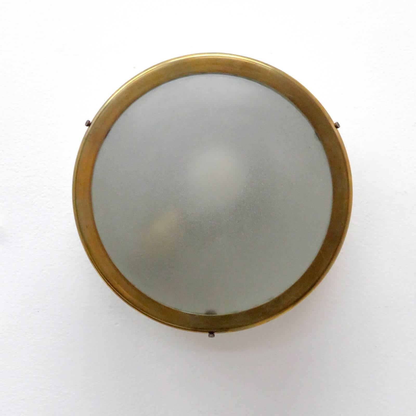 wonderful 1950s flush mount wall or ceiling light, one light source behind frosted glass framed by a brass rim on an egg shell colored, partially perforated aluminum enclosure.