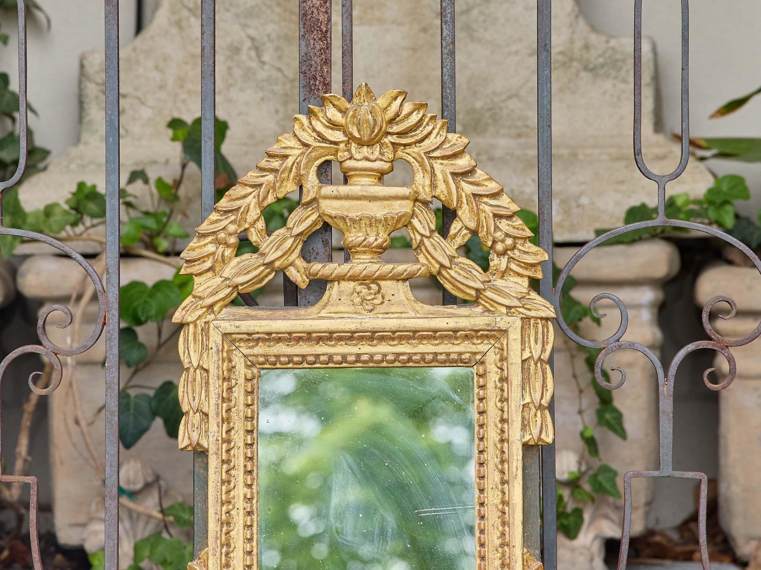 Questo piccolo specchio francese del 1920 circa è un'eco poetica della grandezza neoclassica, intagliato nel legno e impreziosito da una lucente finitura dorata. Con una larghezza di circa 14 pollici, una profondità di 2 pollici e un'altezza di