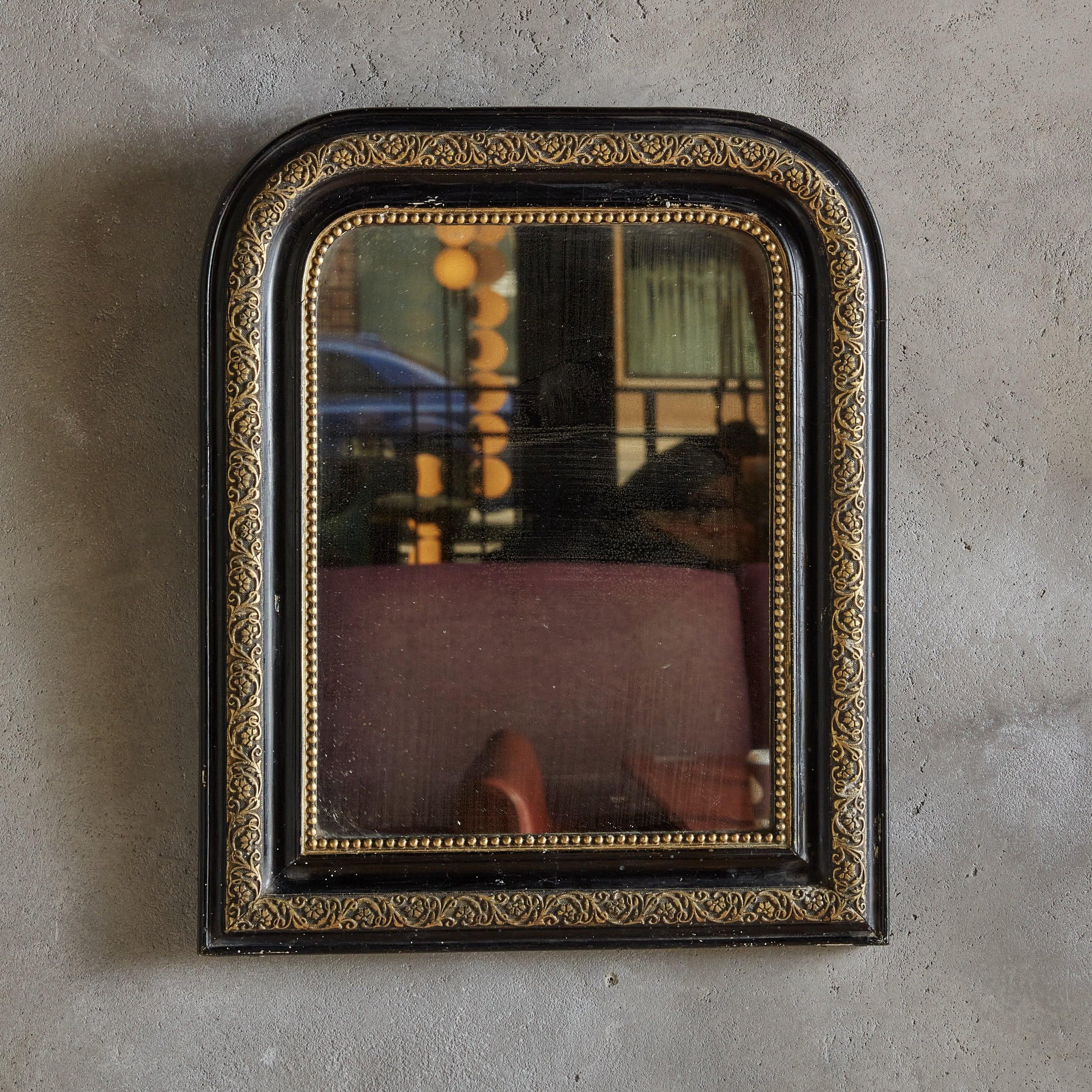 Precioso espejo de pared Louis Philippe de principios del siglo XX procedente del sur de Francia. Este pequeño espejo tiene un marco arqueado de madera pintada de negro, decorado con cuentas doradas y detalles florales. El cristal del espejo se ha
