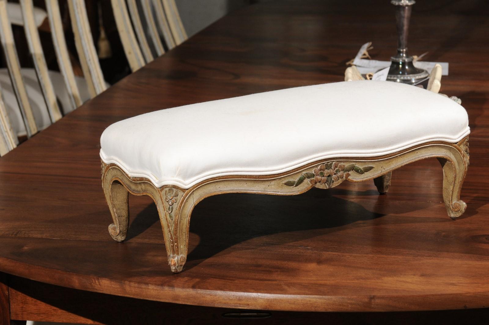 A French Louis XV style Provençal painted wood footstool from the 19th century, with new upholstery and carved accents. Born in Provence during the 19th century, this elegant footstool features a rectangular top covered in a new double welt cotton