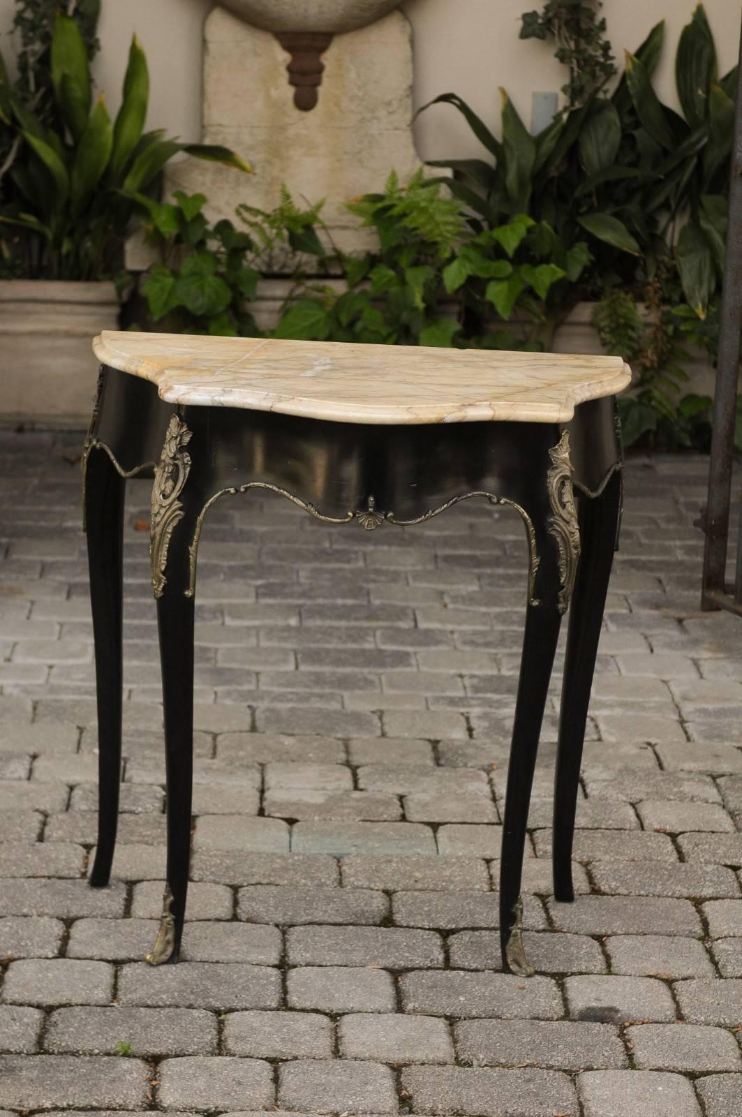 A French Louis XV style ebonized wood petite console table from the early 20th century with serpentine front, marble top and bronze mounts. This exquisite French side table features a beautifully shaped veined marble top with beveled edges, sitting