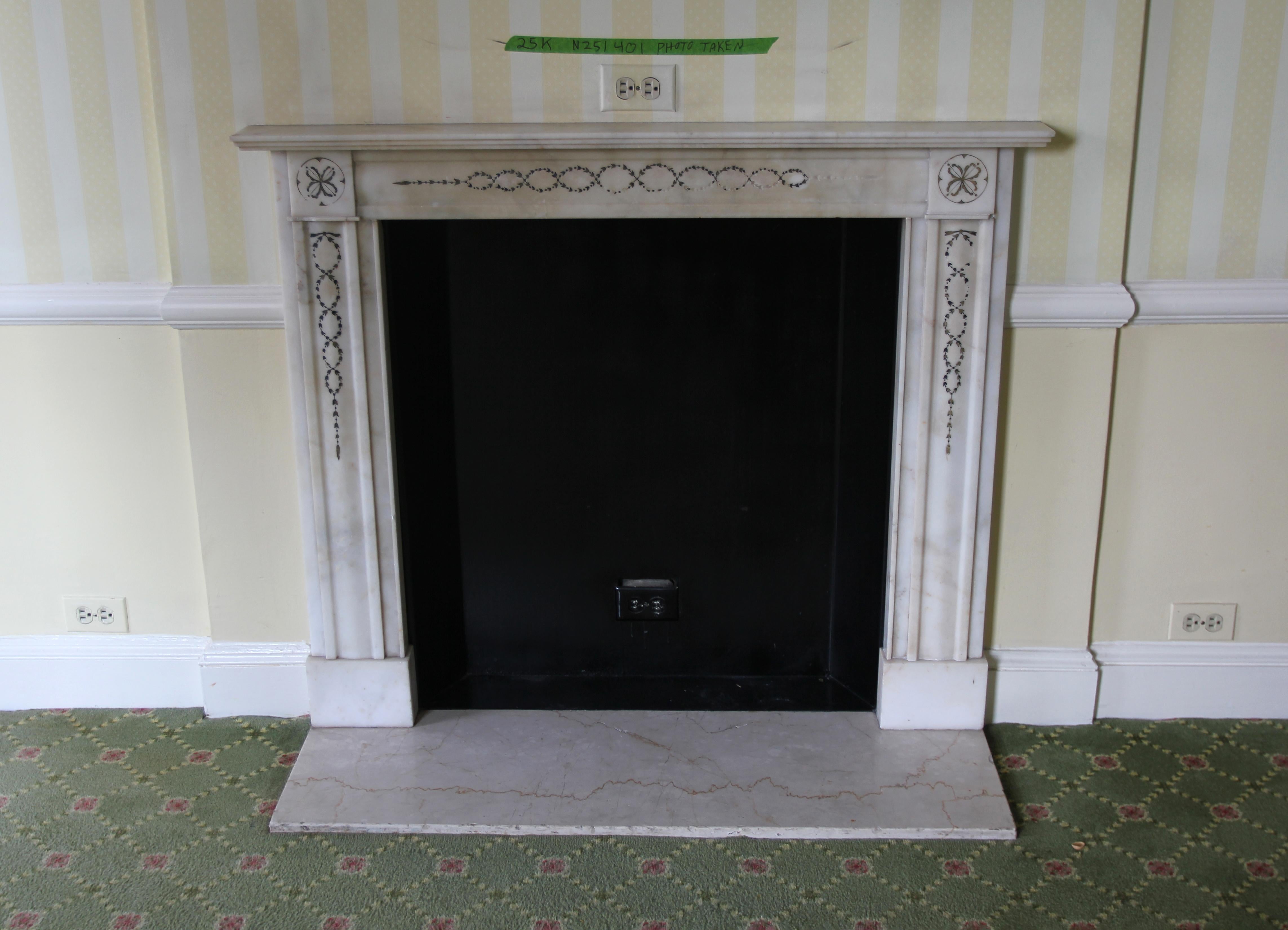 Hearth not included. Small French Regency style white marble mantel with decorative wreath detail on the header, top plinths and the sides. This mantel was one of a group of antique mantels imported from Europe and installed in the Waldorf Astoria
