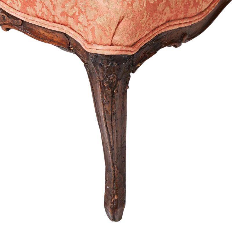 Un petit fauteuil Louis XV avec une tapisserie en damas de soie.  La chaise française en noyer est sculptée avec de magnifiques détails au niveau du dossier incurvé, du tablier de l'assise et des pieds.  Le luxueux revêtement en damas de soie corail