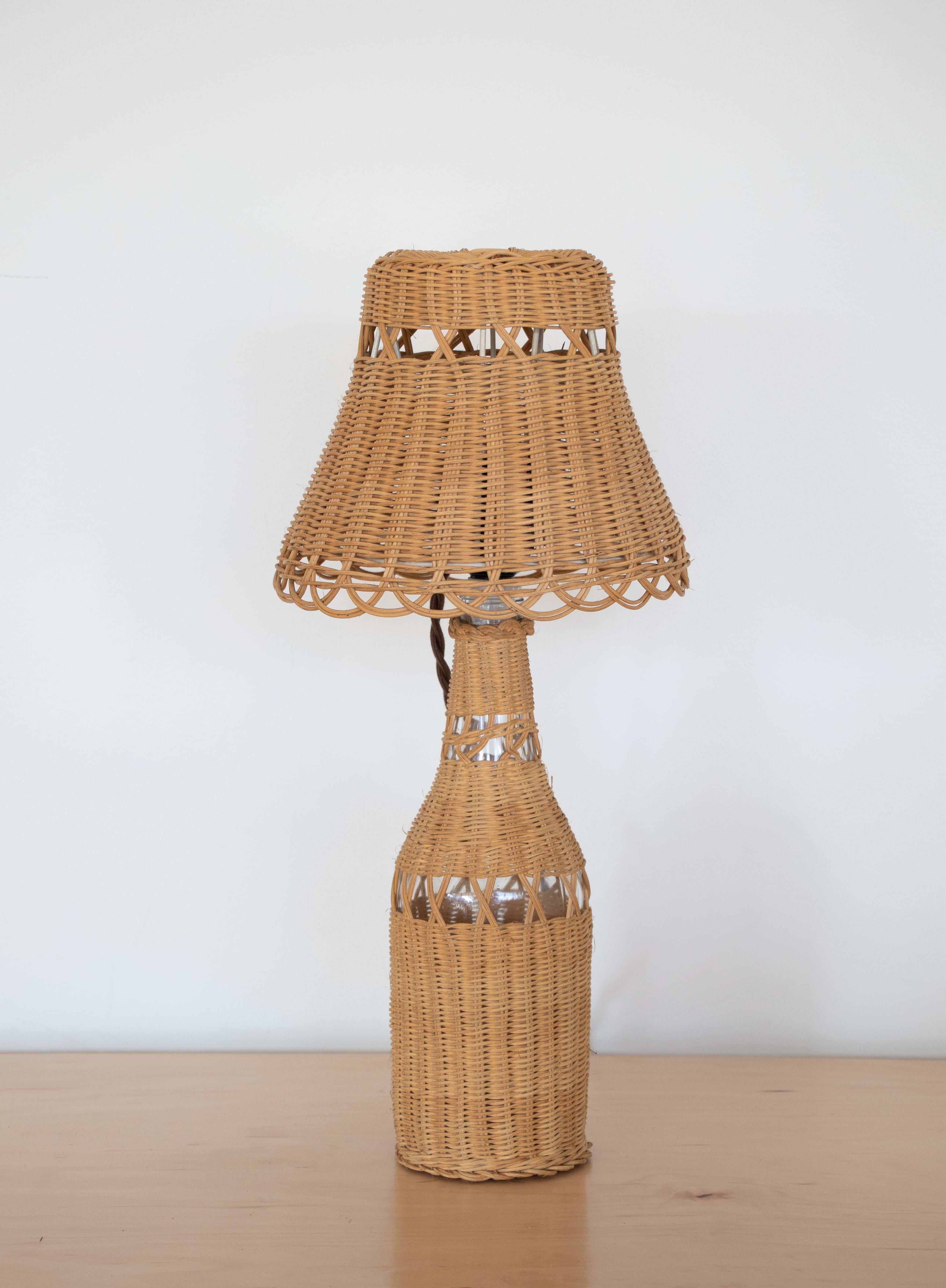 Petite French wicker table lamp with clear glass bottle wrapped in wicker and an all wicker shade. 

Measures: Lamp base diameter 3.5
