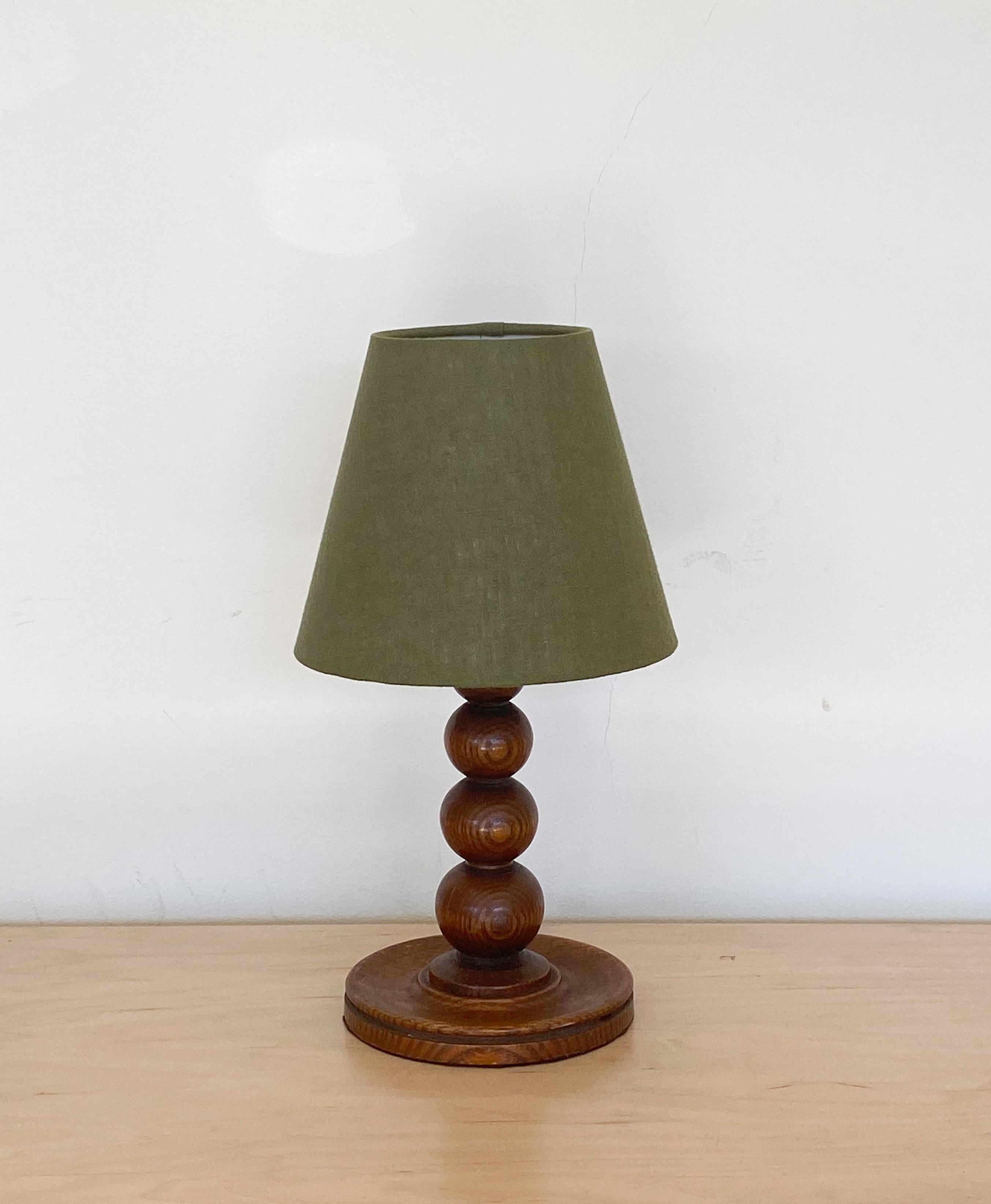 Petite wood table lamp from France, 1940s. Stacked ball forms with circular base and original wood finish. New green linen shade and newly re-wired.

Measures: Shade diameter 7