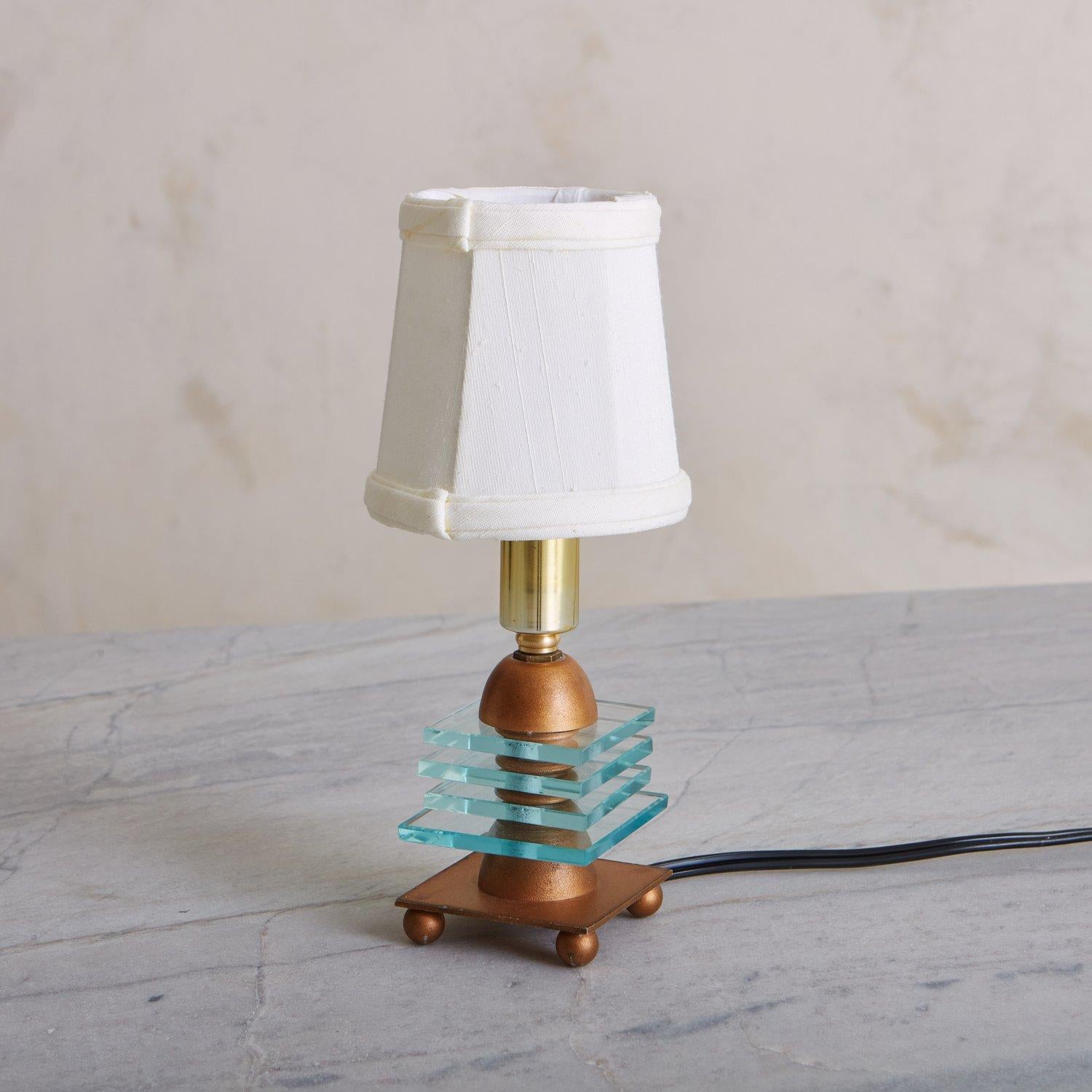 A darling table lamp featuring a sculptural copper tone metal base with four square glass decorative details. It sits on four petite ball feet and has gold hardware. Sourced in France, 20th century.