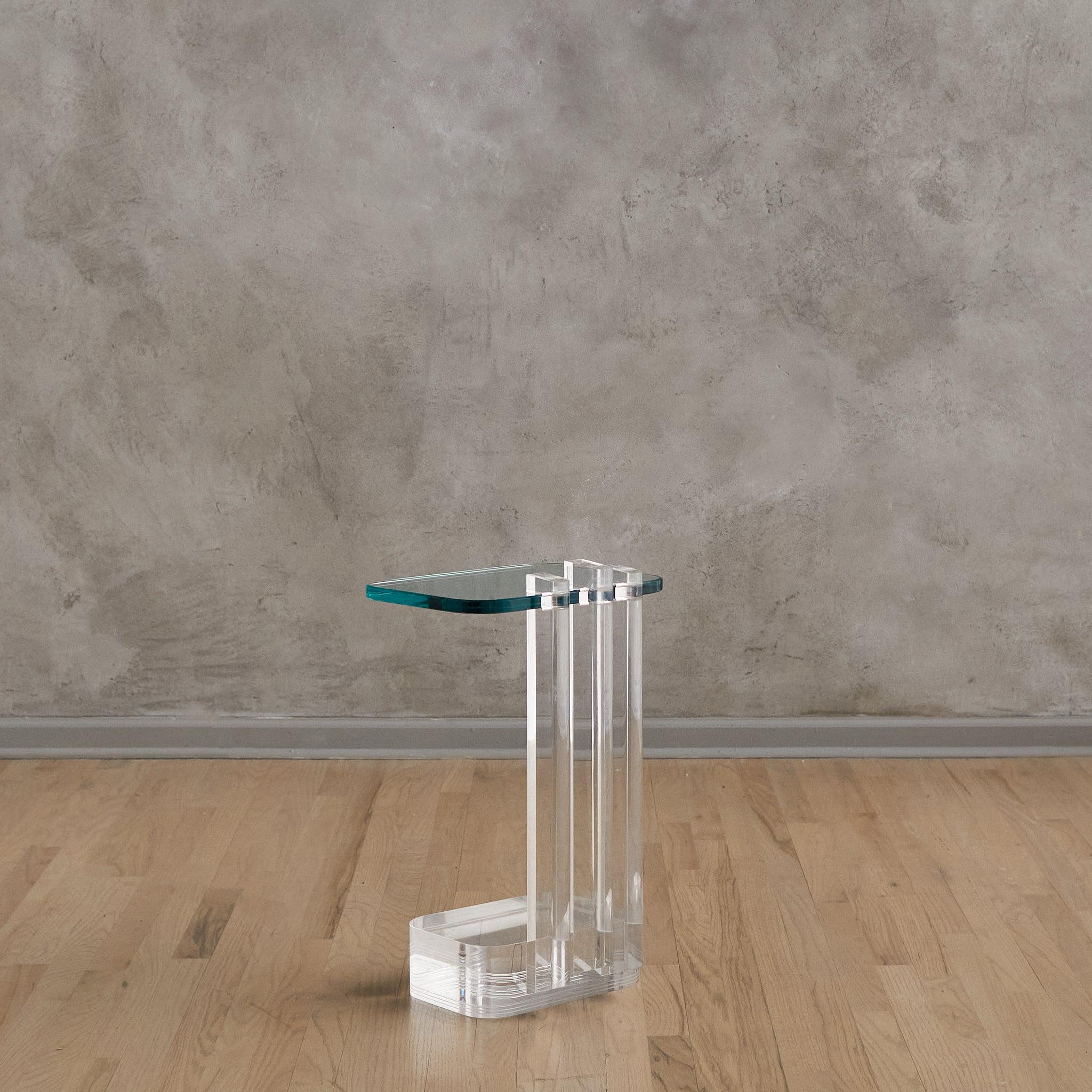 A petite 1980s side table by Les Prismatique, where Art Deco influence meets minimalism. Three lucite columns rise from a weighted clear base, supporting a cantilevered glass top with a polished edge. The transparency plays with light and shadow,