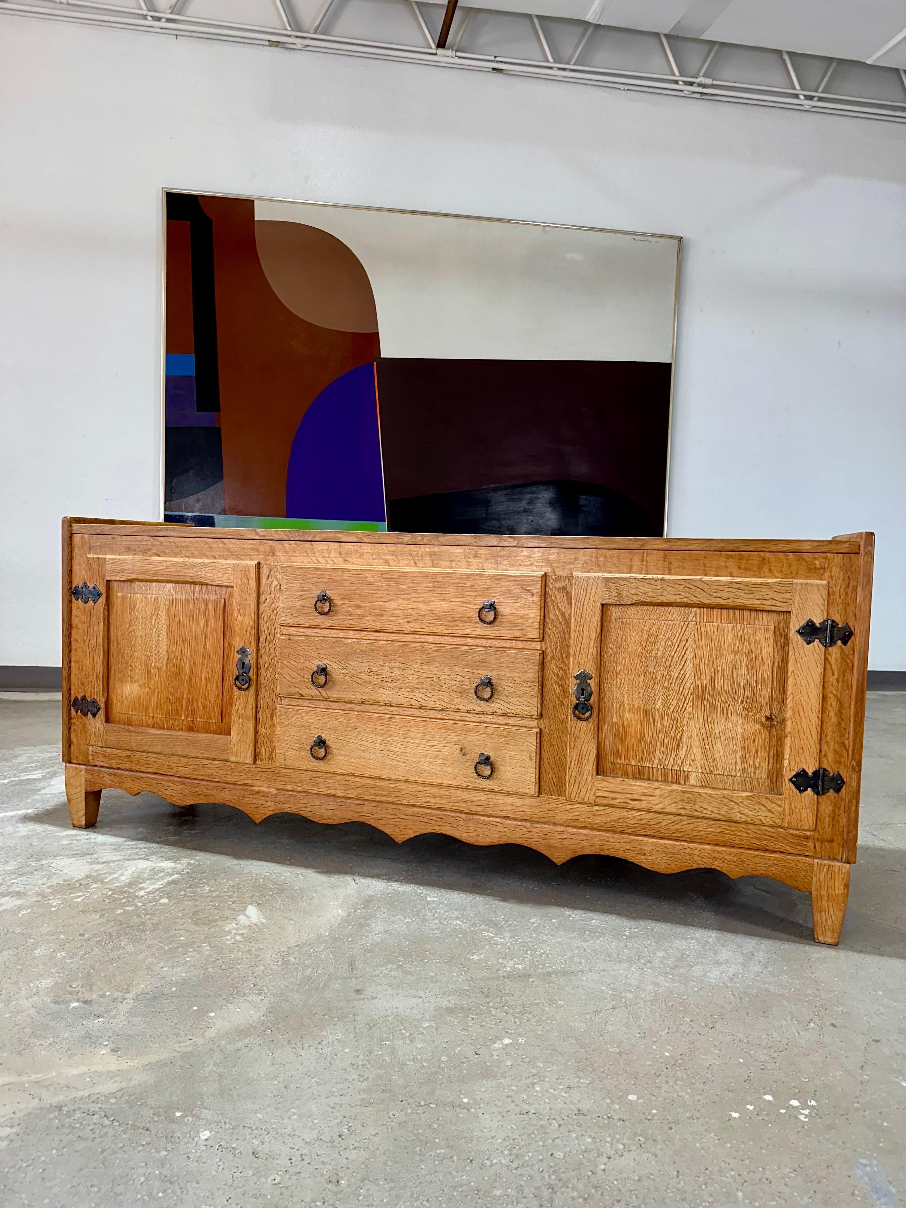Vintage Danish solid oak brutalist sideboard credenza c1970’s attributed to Henning Kjaernulf. Carved panels on locking doors at left and right with iron hinges open to one shelf on each side. Center features three  drawers with iron clover and ring