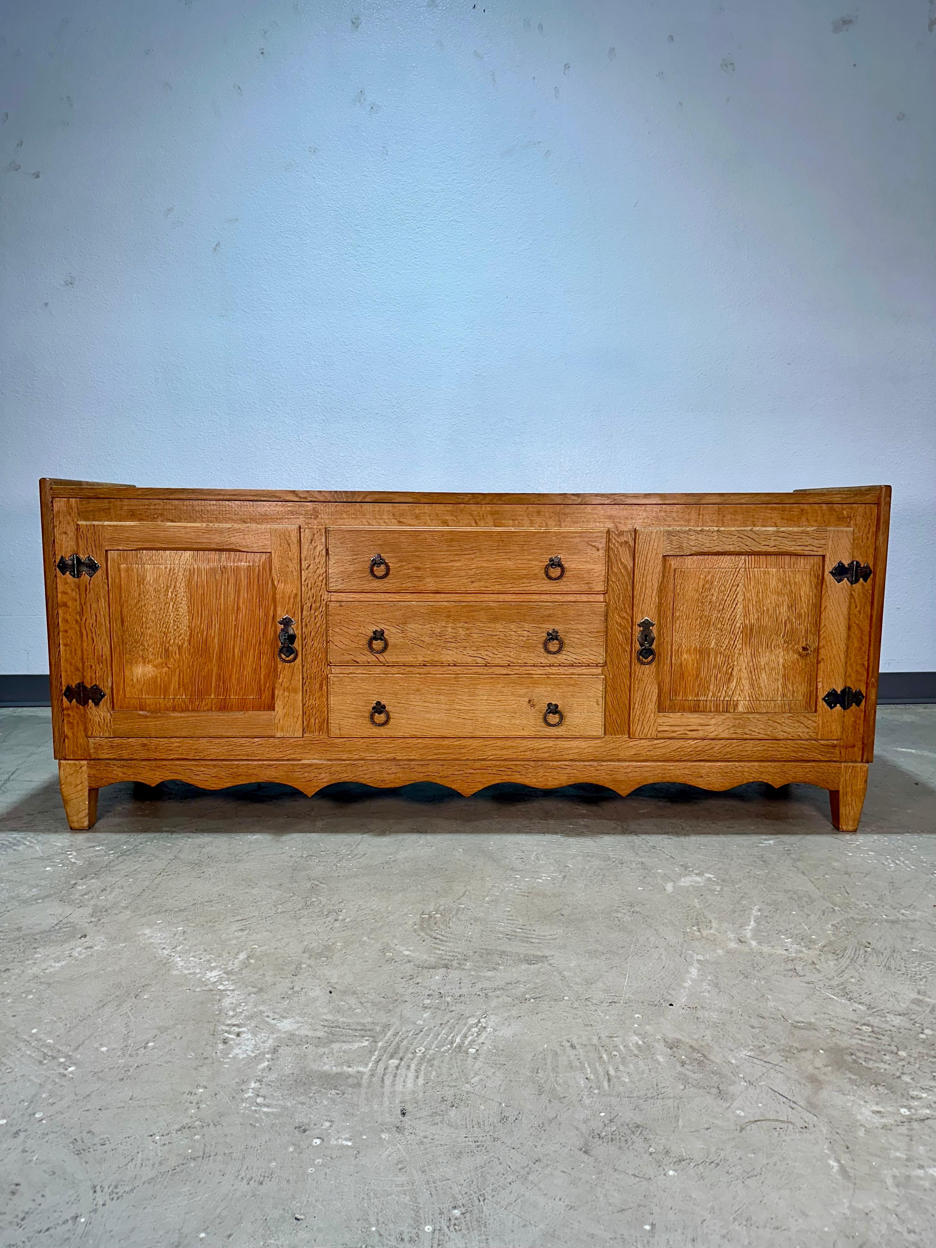 Vintage Danish solid oak brutalist sideboard credenza c1970’s attributed to Henning Kjaernulf. Carved panels on locking doors at left and right with iron hinges open to one shelf on each side. Center features three  drawers with iron clover and ring
