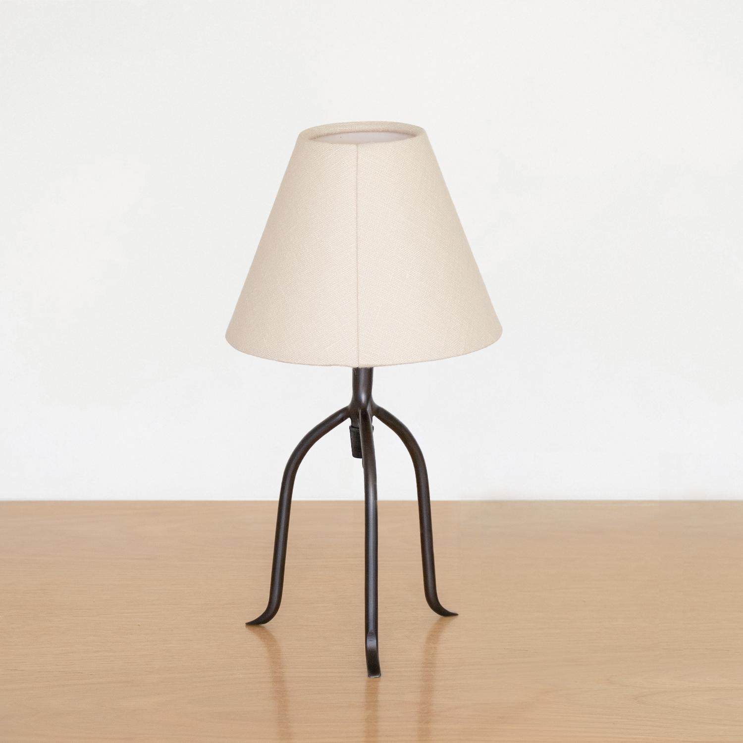 Petite iron tripod lamp with slender legs and tapered feet. New wiring and new oyster linen shade. Multiple available, sold individually. Takes one E12 base bulb, up to 25 W or higher using LED.