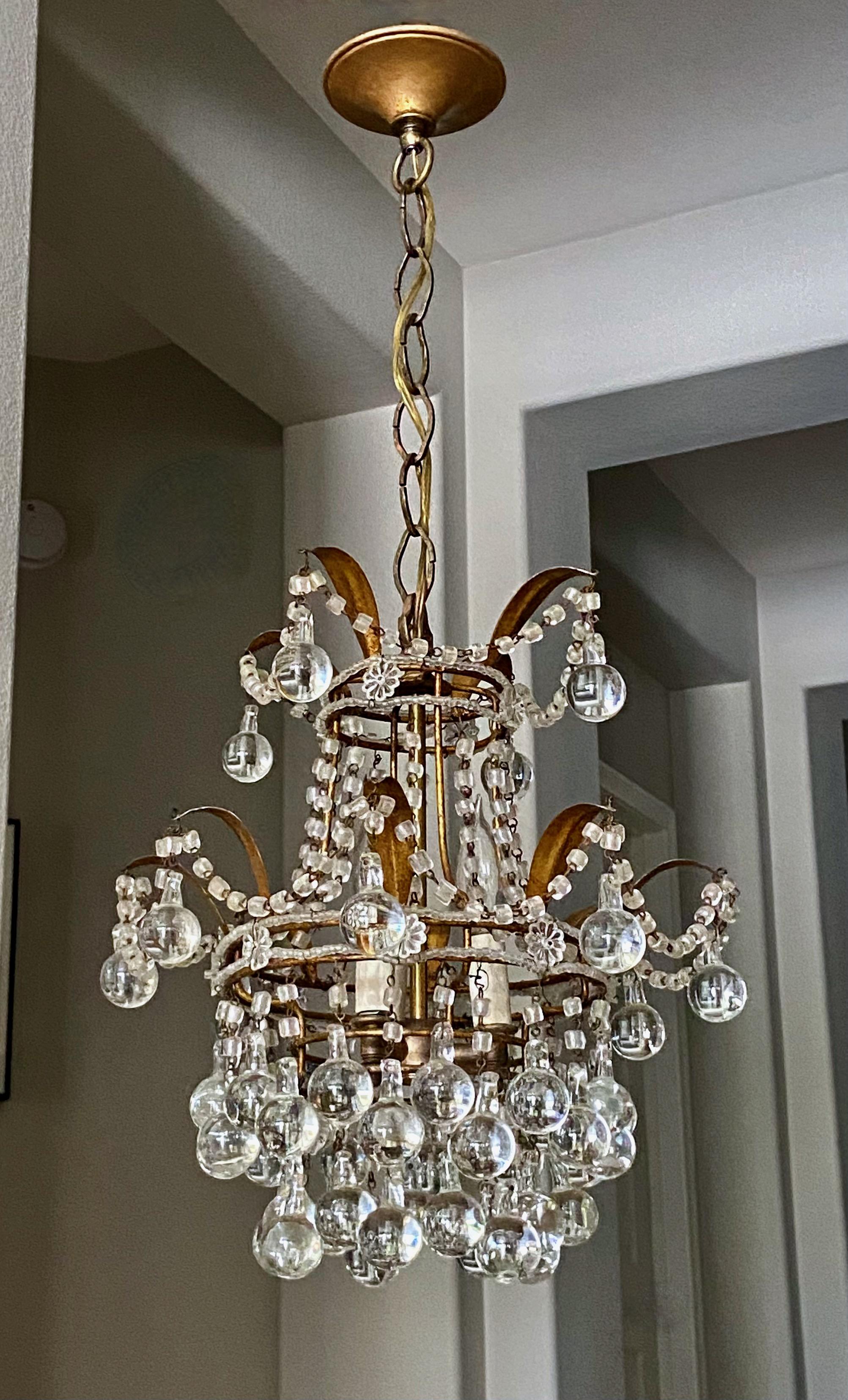 Petite scale Italian gilt metal tole chandelier pendant light. Covered with macaroni beaded swags, florets and crystal Murano drops. Uses 3 candelabra B base bulbs. 
The fixture measures 14