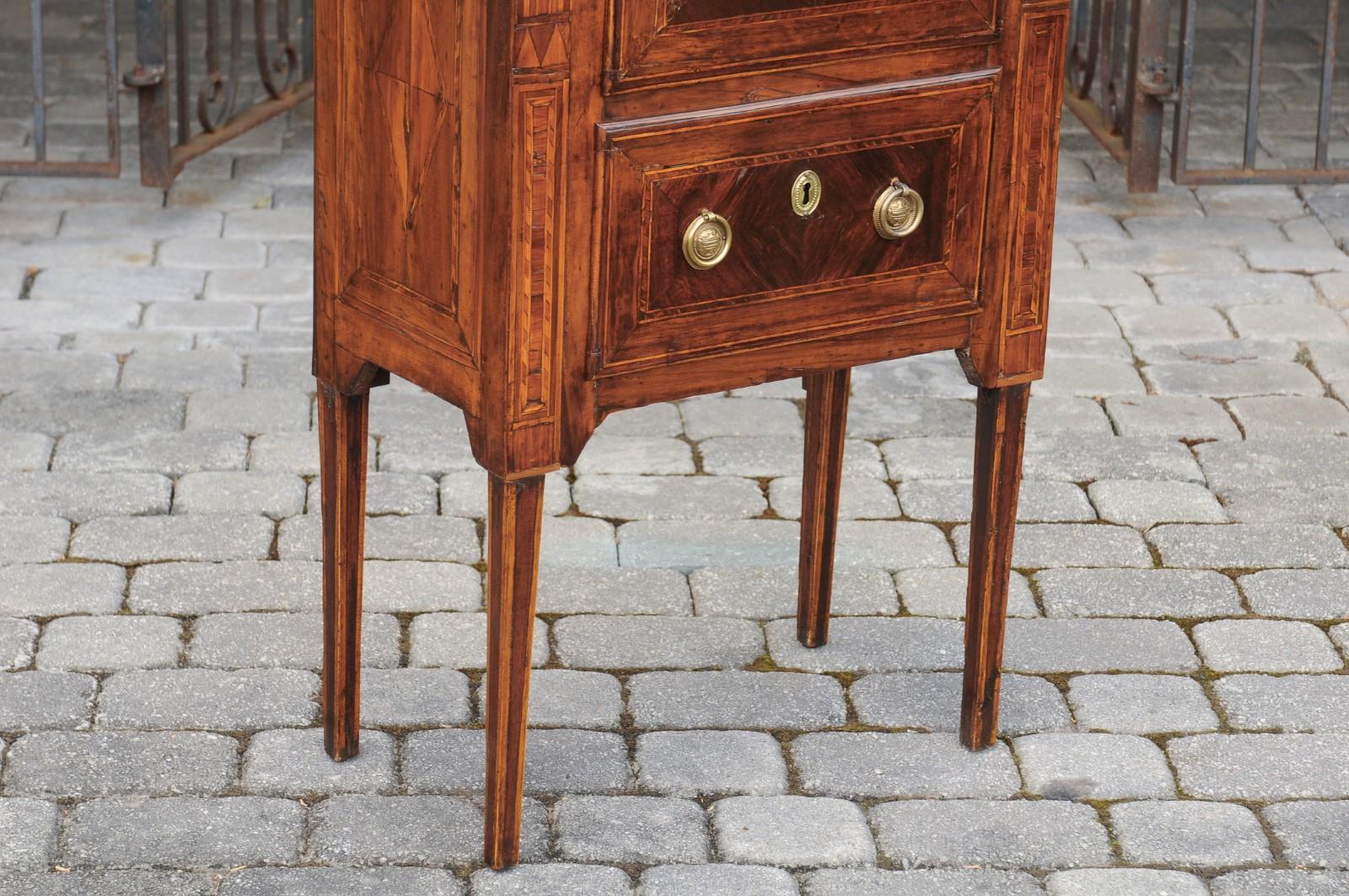 A petite Italian neoclassical period walnut commode from the early 19th century, with inlaid motifs and two drawers. Born in Italy during the early years of the 19th century, this exquisite Italian commode features a rectangular top adorned with an