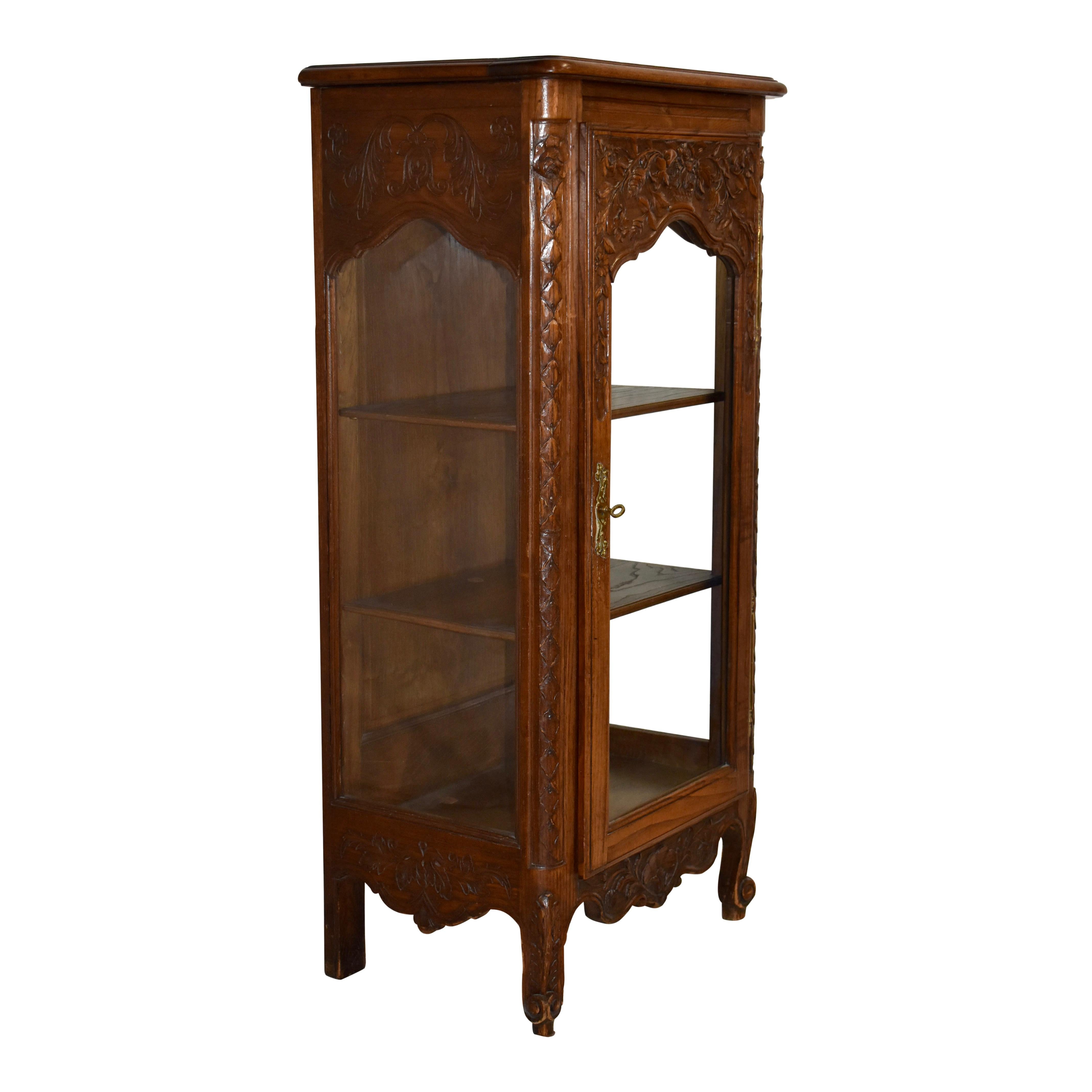 Beauty abounds in this petite carved vitrine from the late-19th century. Crafted from European Oak with a medium finish that does not hide the oak's beautiful grain, the vitrine features a floral motif with carvings of roses on the door and at the