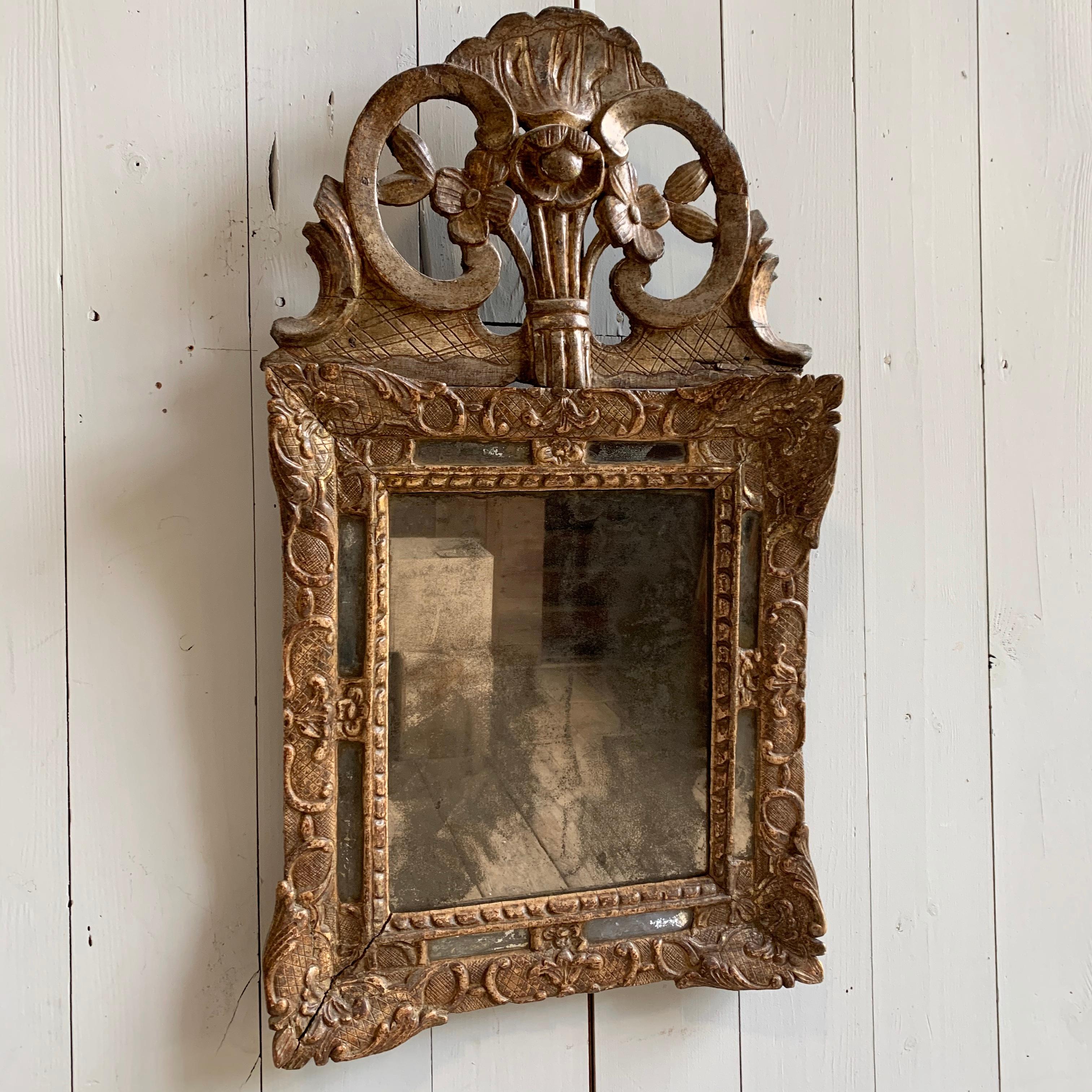 A petite Louis XV period mirror with carved and embossed decoration with an upper crest over a rectangular glass plate, circa 1760, France.