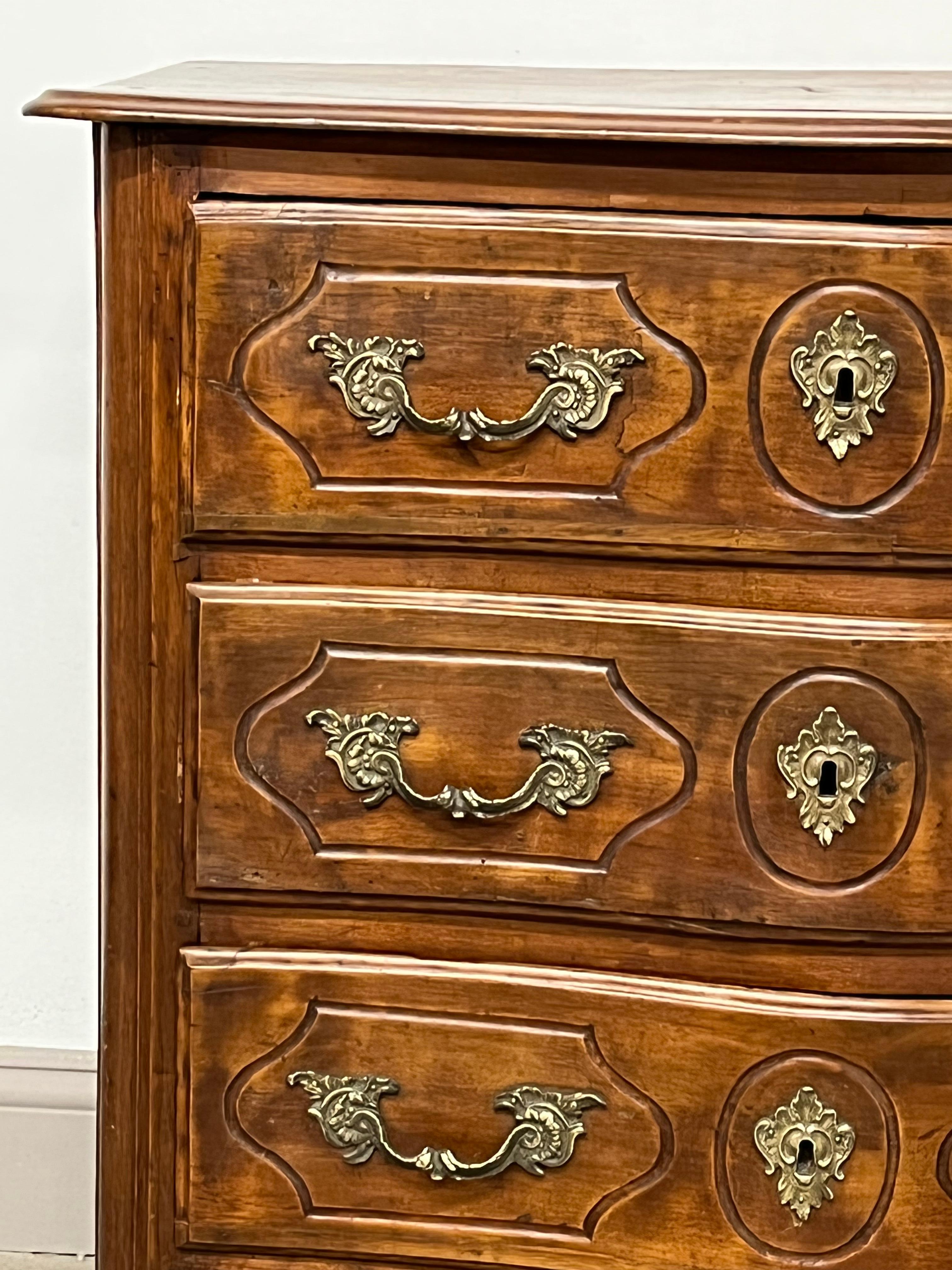 A petite Louis XV period 3-drawer commode with slightly serpentine front, the carved drawers retaining their original brass hardware, with a conforming wood top and simple straight legs. An unusual small size, popular today as a bedside cabinet.