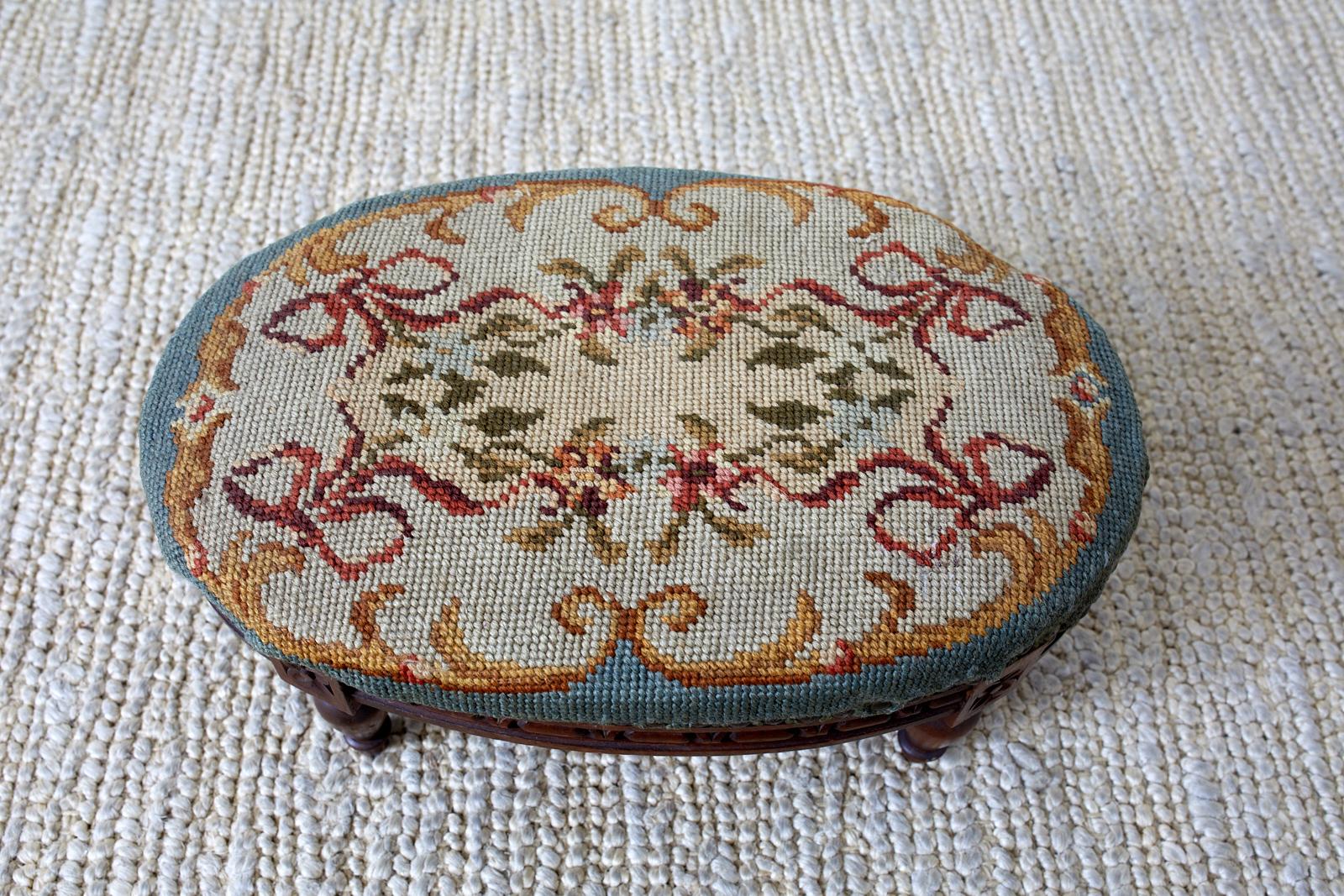 19th century carved walnut oval footstool made in the Louis XVI taste. Featuring a needlepoint upholstery and brass nailhead trim. Intricately carved apron with turned legs.
 