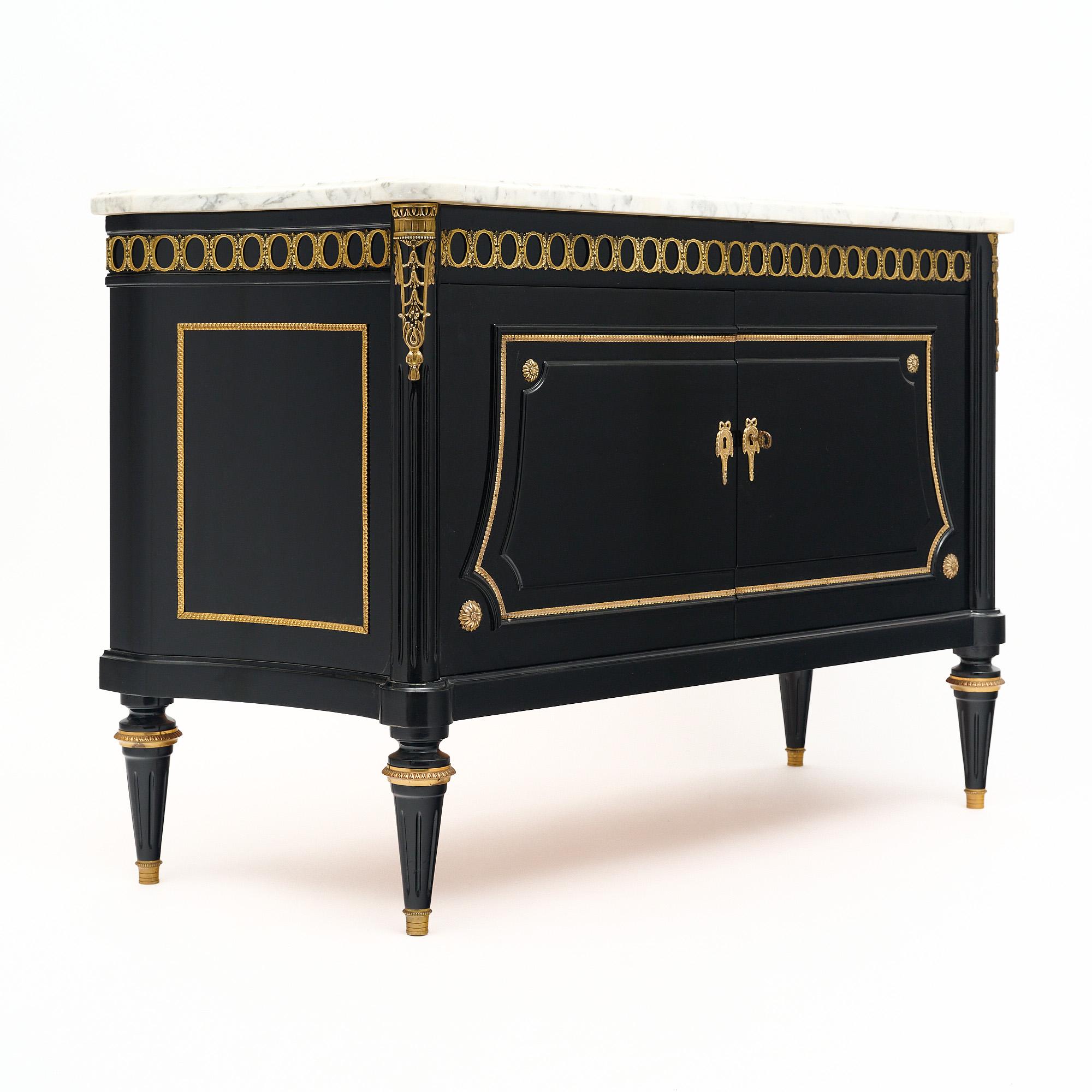 Small buffet in the Louis XVI style from France. This piece has been ebonized and finished with a lustrous museum-quality French polish with gilded ormulu throughout. Two doors open to interior shelving and the whole case piece is adorned with gilt