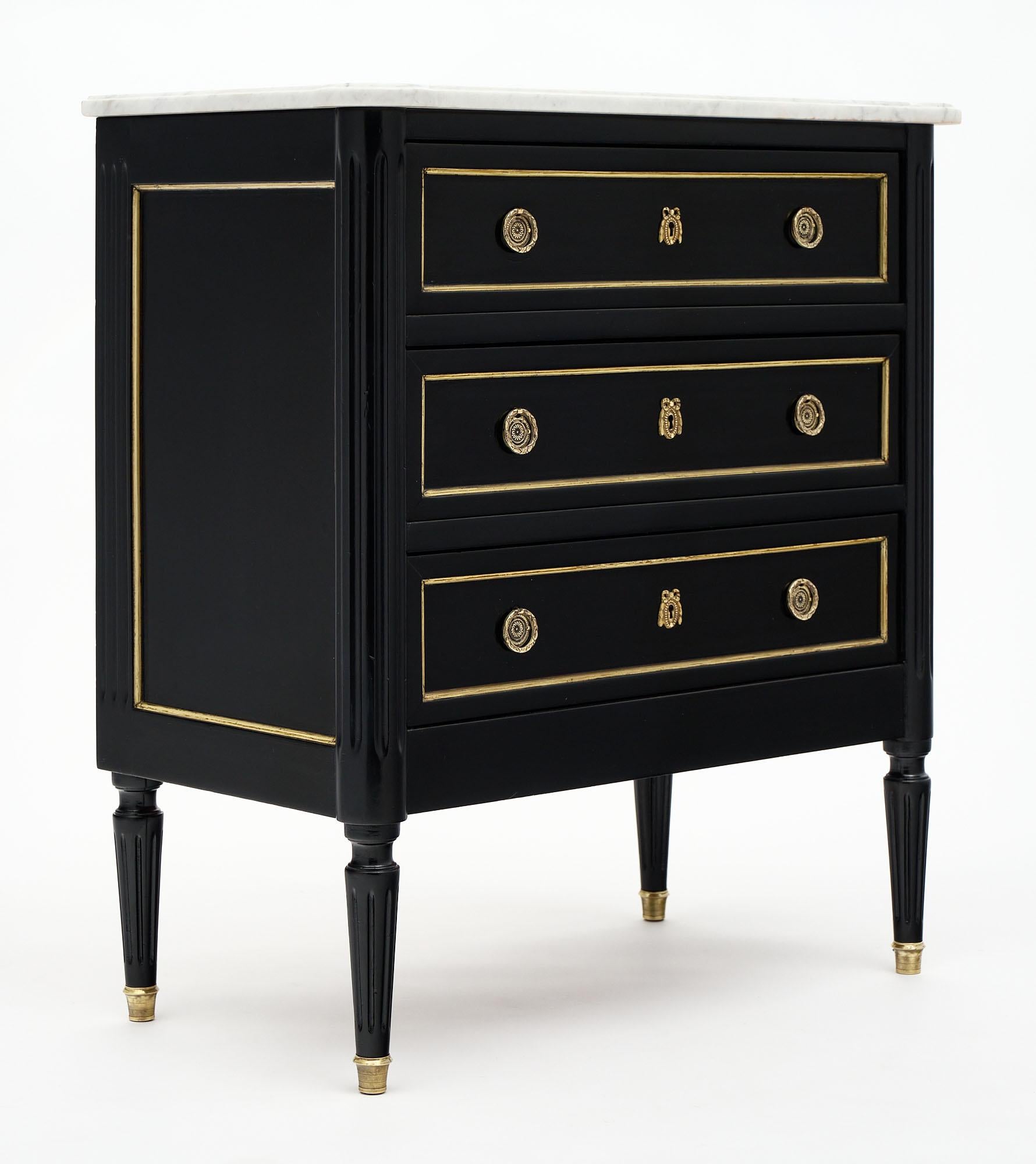 Petite Louis XVI style French chest of drawers made of solid mahogany and finished in a lustrous French polish and ebonized. This piece is topped with a Carrara marble slab and features gilt brass trims and hardware throughout. We love the small;