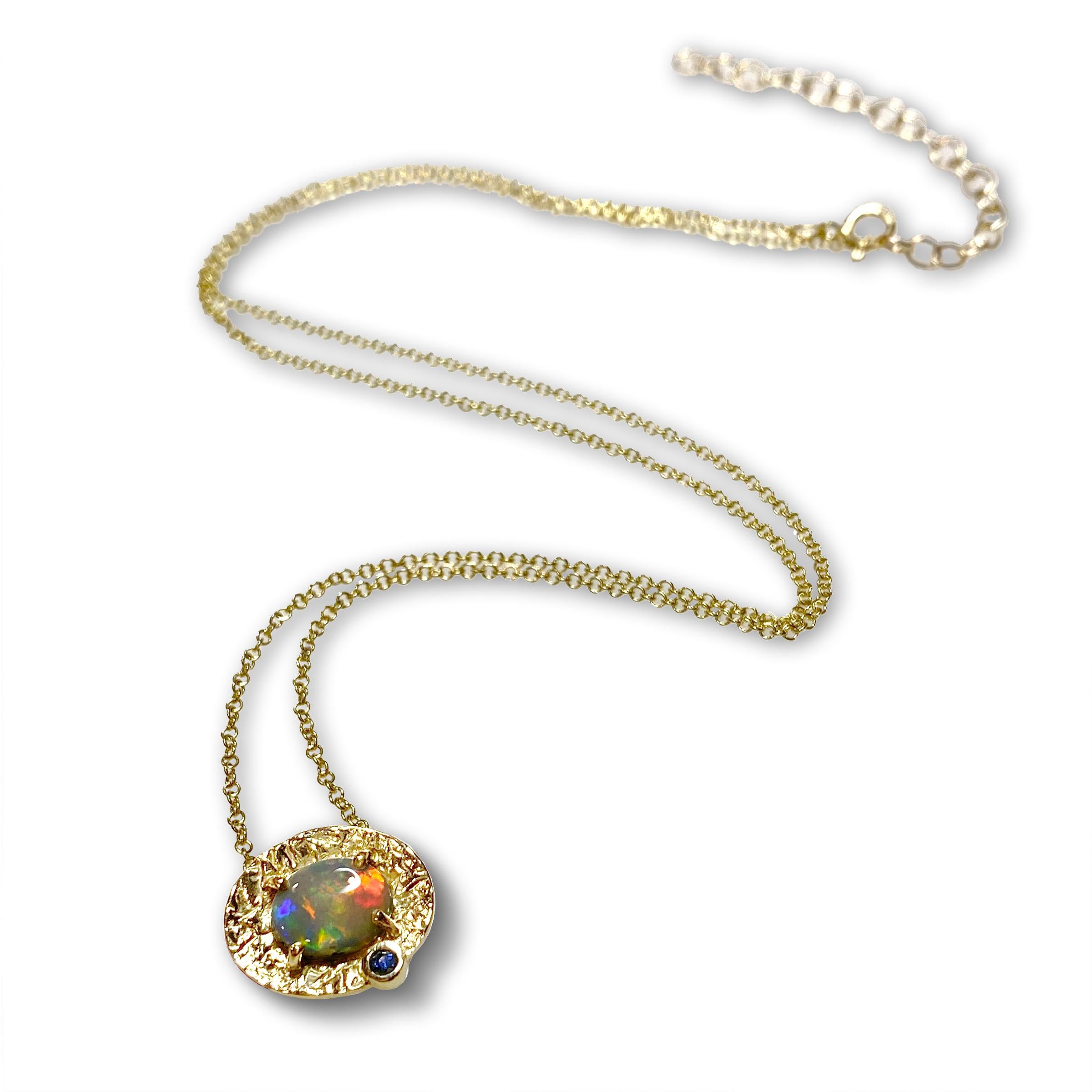 Le collier unique Petite Marigold de Keiko Mita est fabriqué à la main à partir d'une opale australienne multicolore (0,69 carats) sertie dans une monture texturée en or jaune 14 carats, rehaussée d'un saphir bleu. Cette magnifique opale, qui