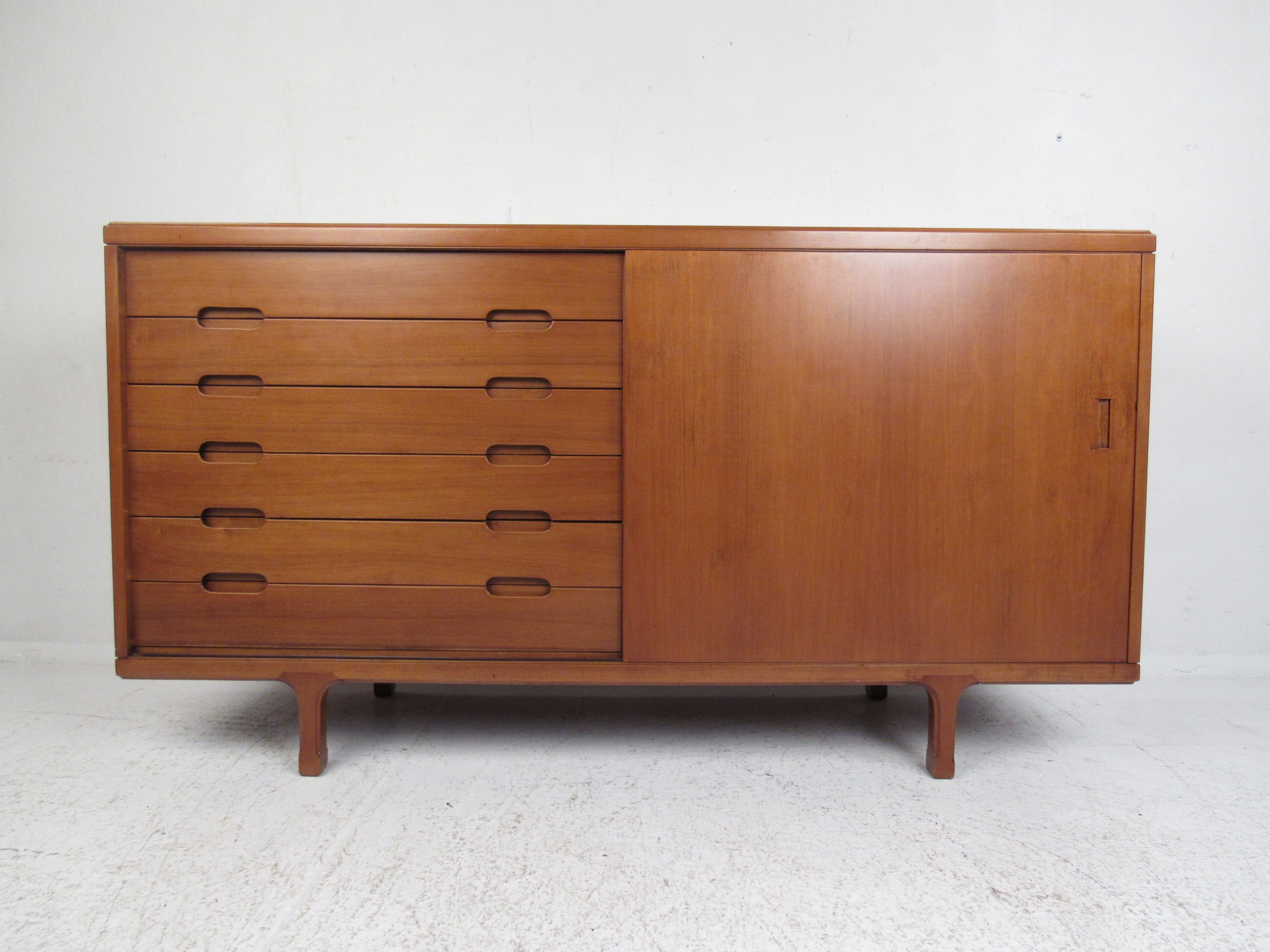 This beautiful vintage modern sideboard boasts sculpted legs and oval recessed drawer pulls. A compact design with six hefty drawers and a large open compartment hidden by a sliding door. This stylish case piece has a charming vintage finish and