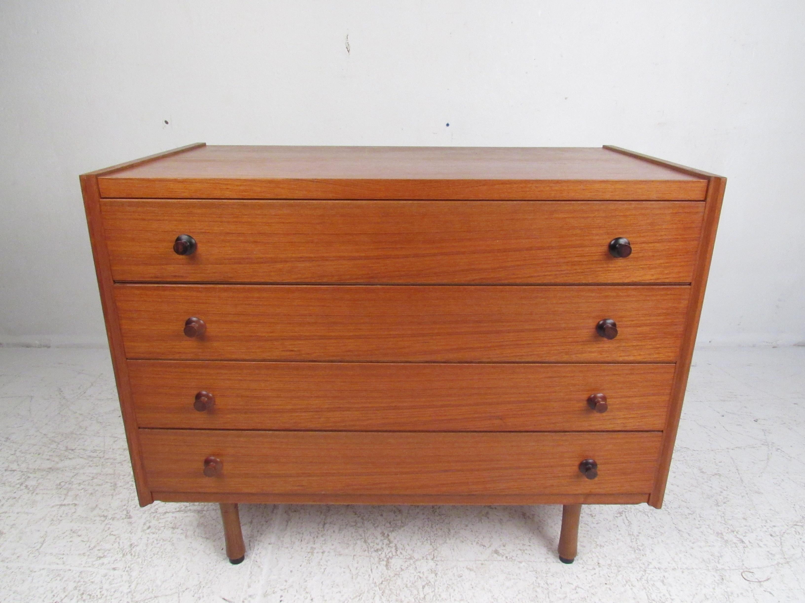 This handsome Danish modern chest boasts conical rosewood pulls, a finished back, and a rich teak wood grain. A compact design with four hefty drawers that ensures plenty of room for storage. The straight line design sits on top of four unusually