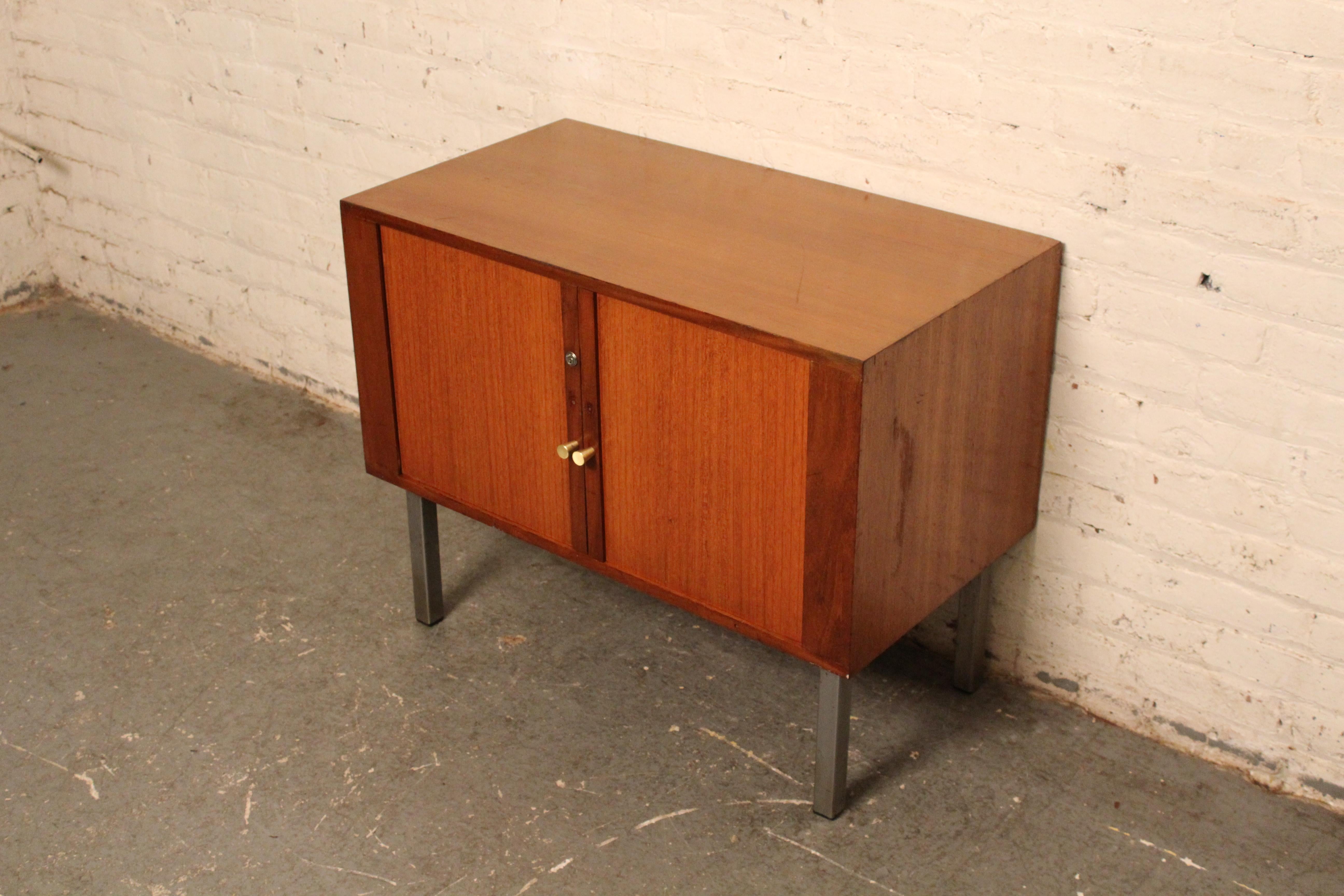 Add a big splash of mid-century modern charm into any room with this compact tambour cabinet! Readily showing design influence from the legendary works of Florence Knoll, it features a simple box silhouette supported by minimalist chrome legs. The