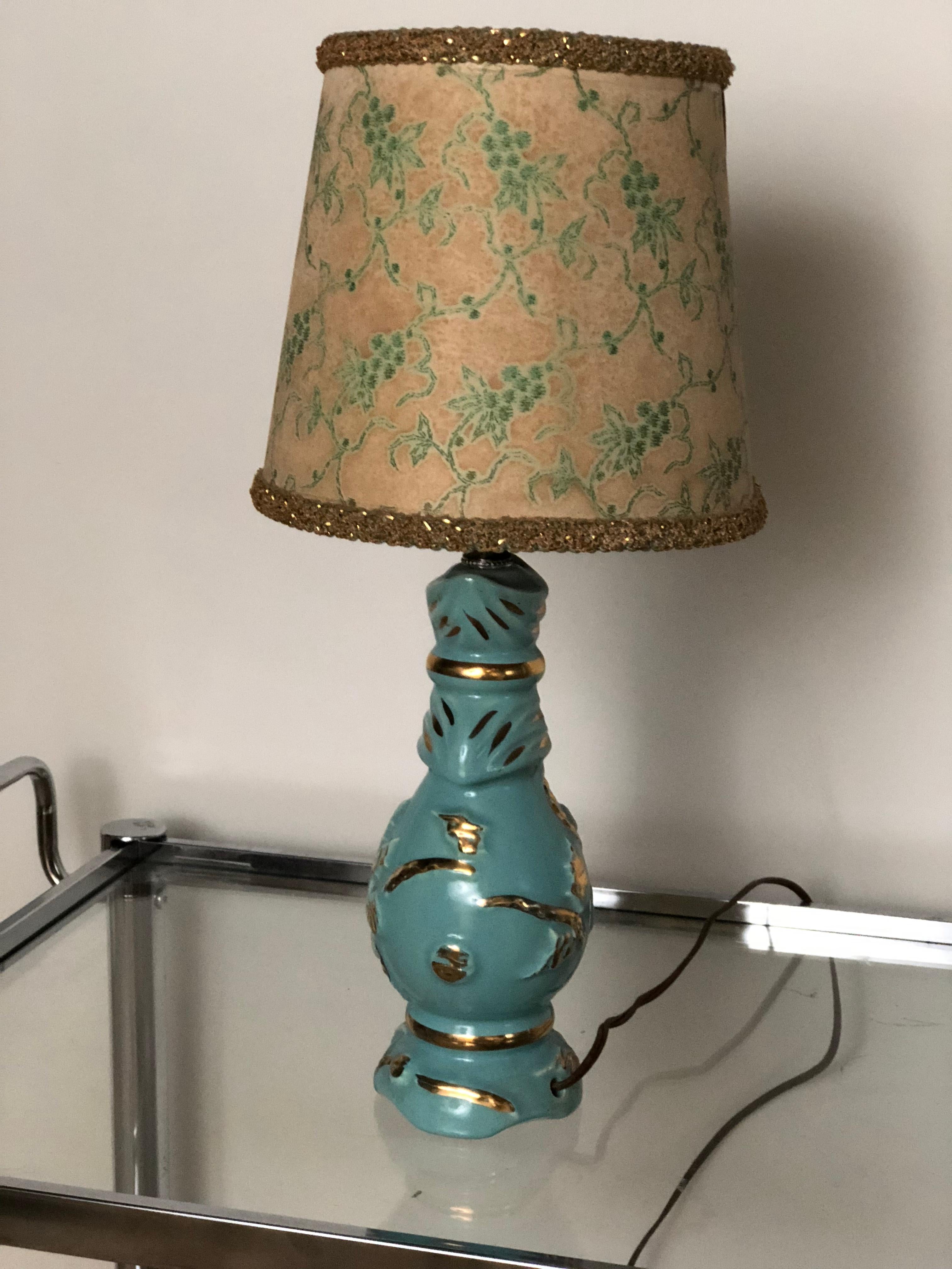 A Classic 1960s petite midcentury ceramic lamp in turquoise with gold decorative accents. The lamp's original paper shade has turquoise floral motifs and gold foil trim around the top and bottom.