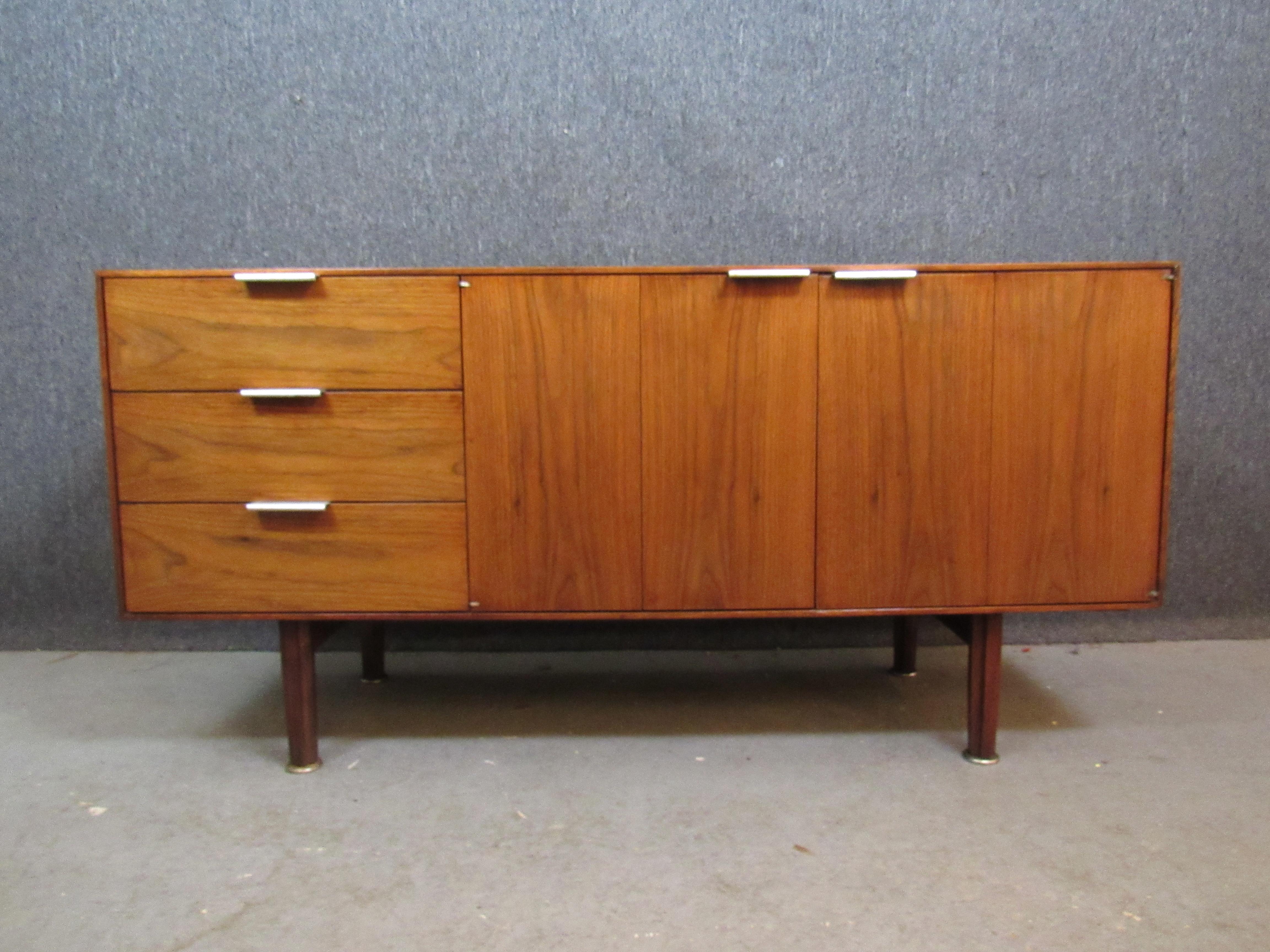 Wonderful compact vintage sideboard from Michigan's John Stuart Inc. of Grand Rapids.  Three pull-out drawers alongside a pair of folding double doors offer plenty of storage space, whether in the home or office. A gorgeous natural wood grain has