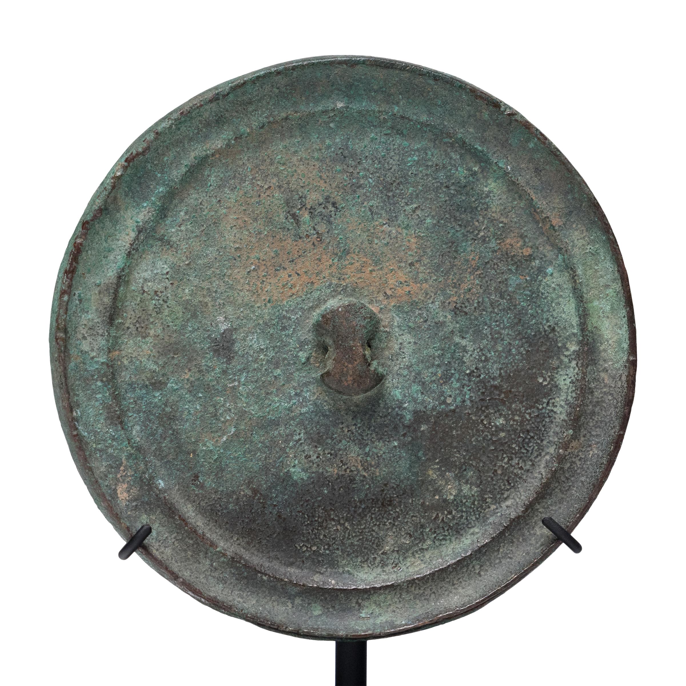 Cloaked in rich patina and verdigris oxidization, this petite Chinese bronze mirror has the simple beauty and undeniable texture of an ancient object. Though an exact date is unknown, the mirror's round form, double ring edge and unadorned surface