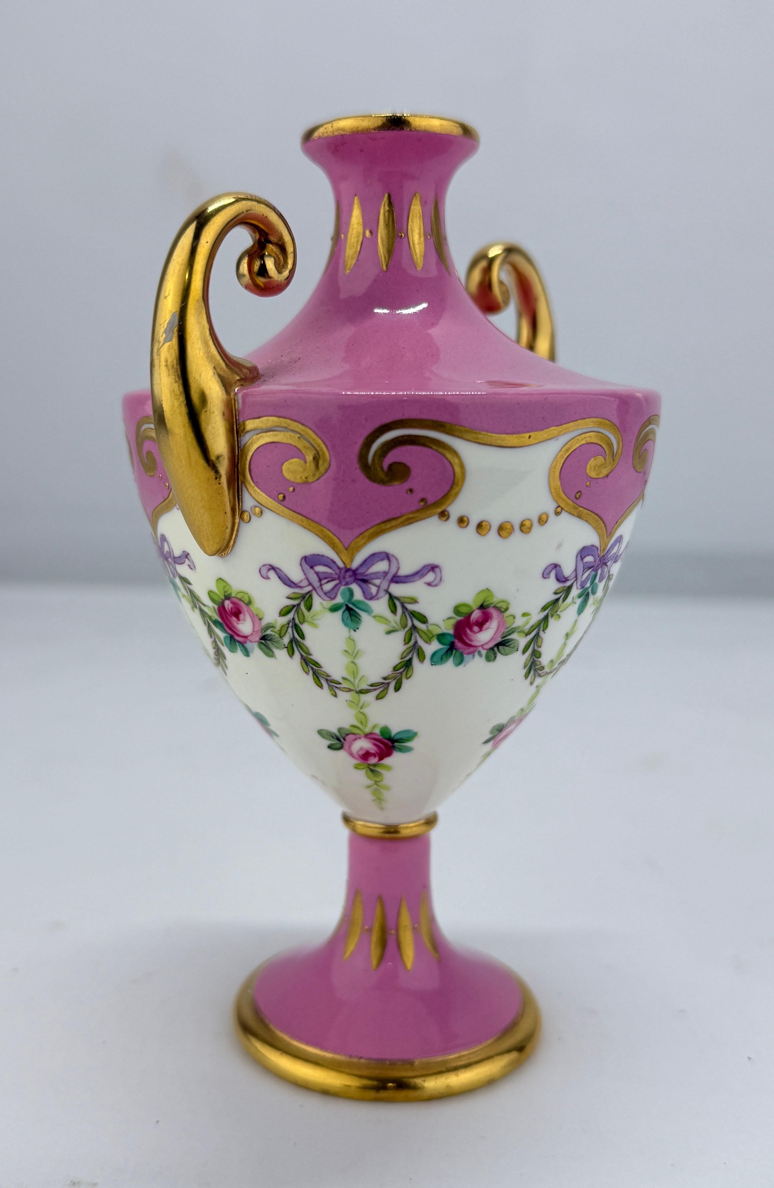 Questo squisito vaso da armadio di Minton, risalente al 1891 circa, è un raffinato esempio di design di ispirazione neoclassica. Realizzato in porcellana, il vaso presenta un elegante fondo magenta, impreziosito da delicati dettagli dorati e motivi