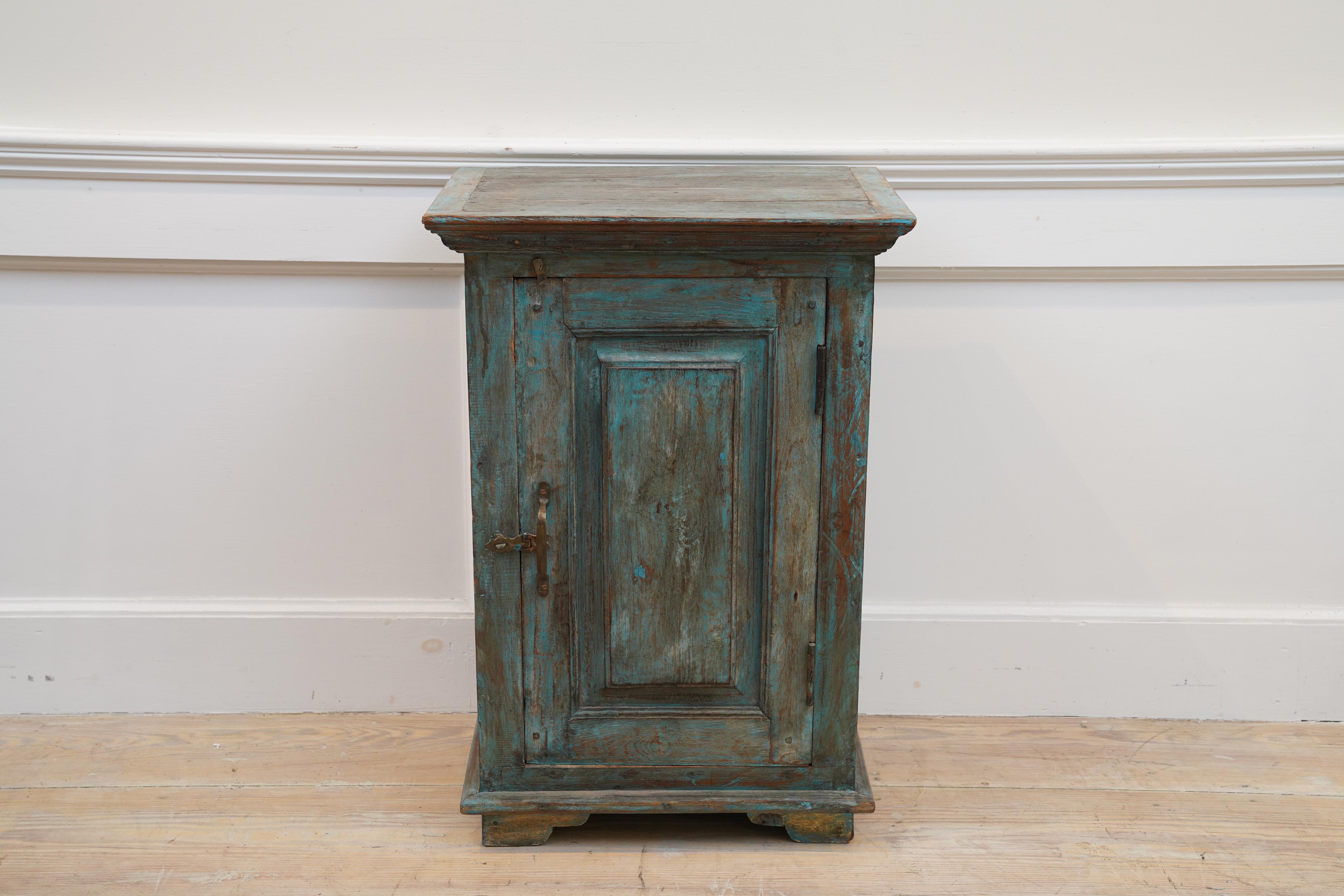 A petite teak cabinet with original blue/green paint. Raised panel door front, carved top moulding, interior shelf and brass hardware. Just the body portion measures 12.5